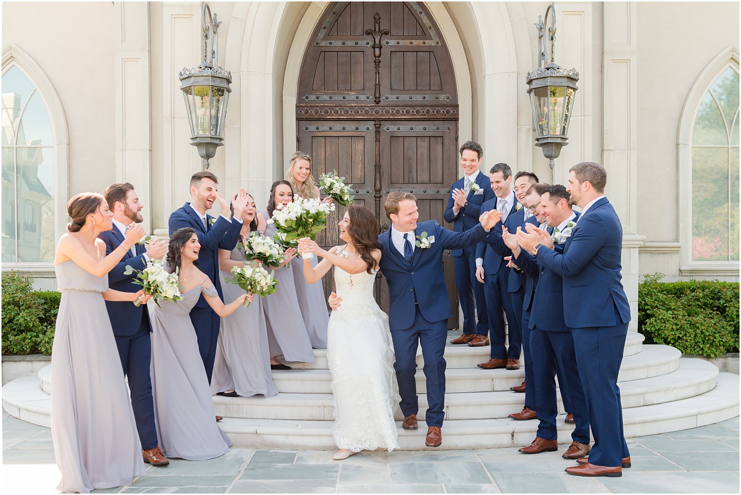 bride and groom stand on steps of chapel at Park Chateau with wedding party