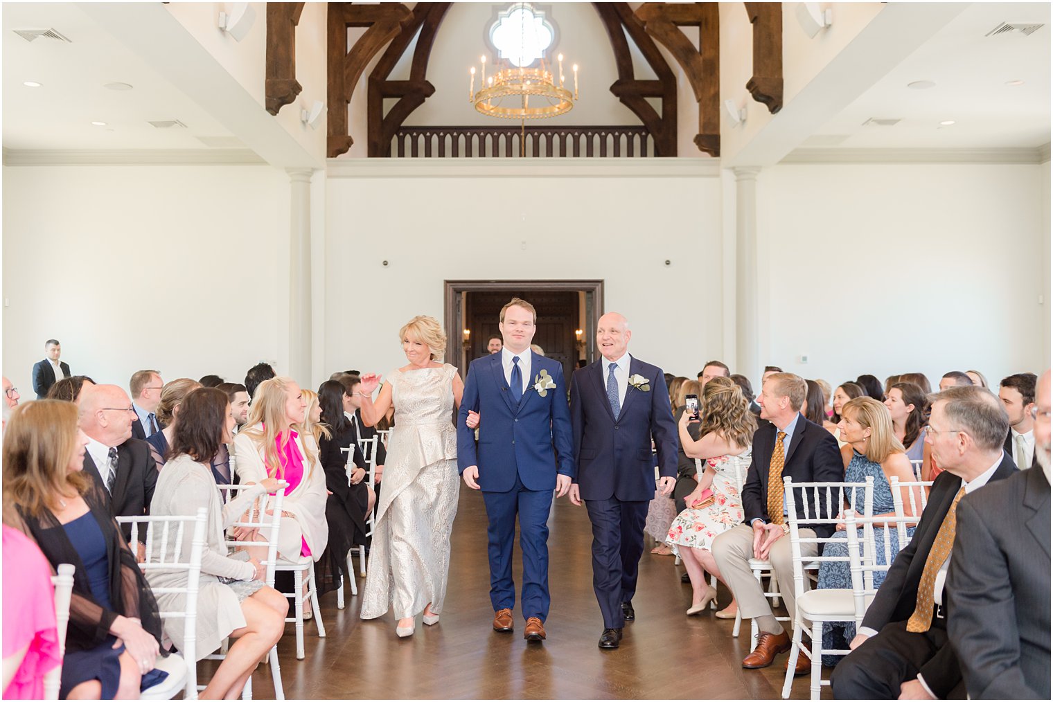 groom walks down the aisle with both parents for wedding ceremony in Park Chateau chapel