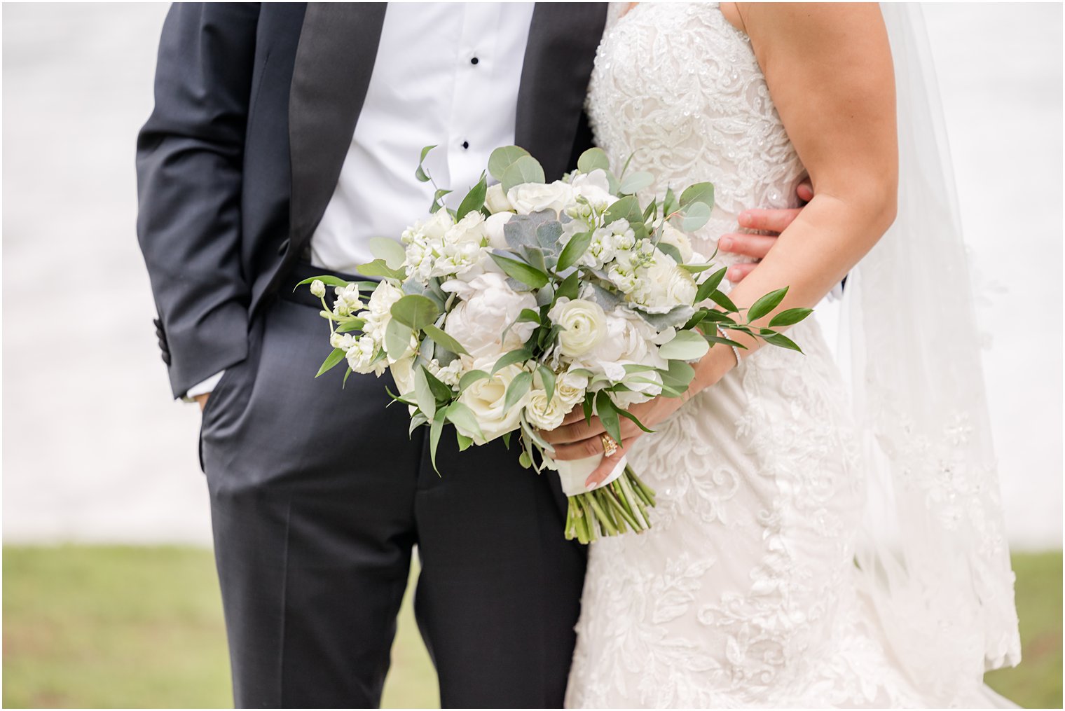 groom hugs bride while she holds bouquet of ivory flowers