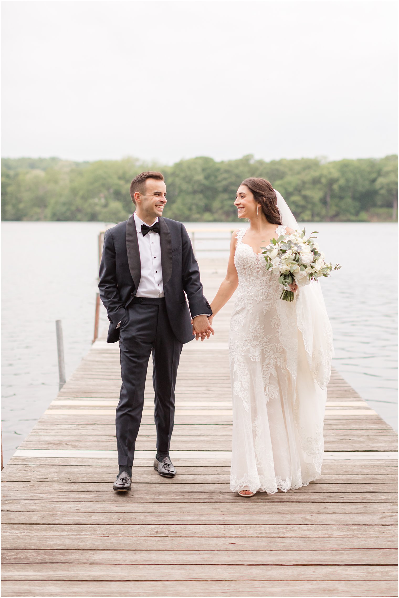 bride and groom hold hands walking on dock