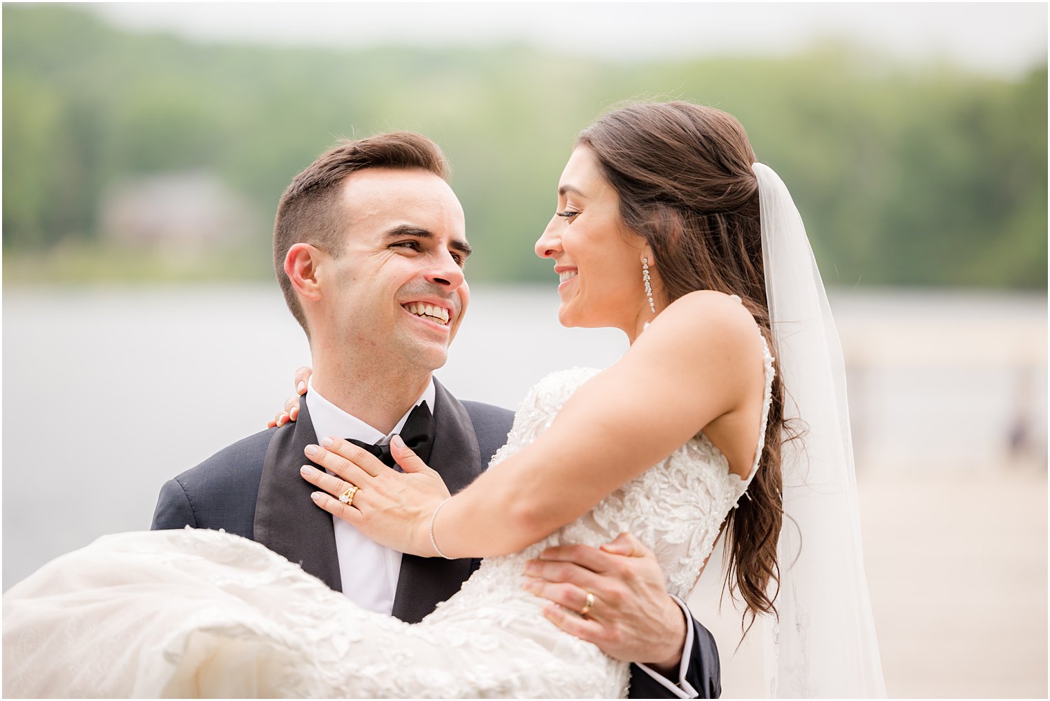 groom lifts bride up during photos by lake