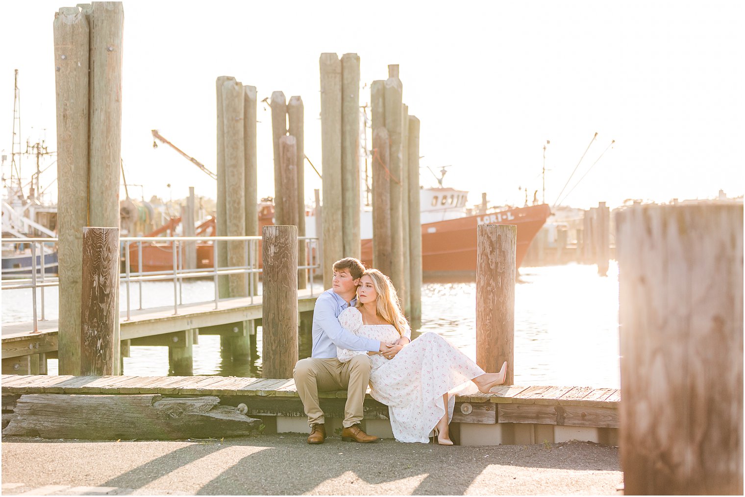 bride and groom sit on wooden pier at sunset during photos at Long Beach Island