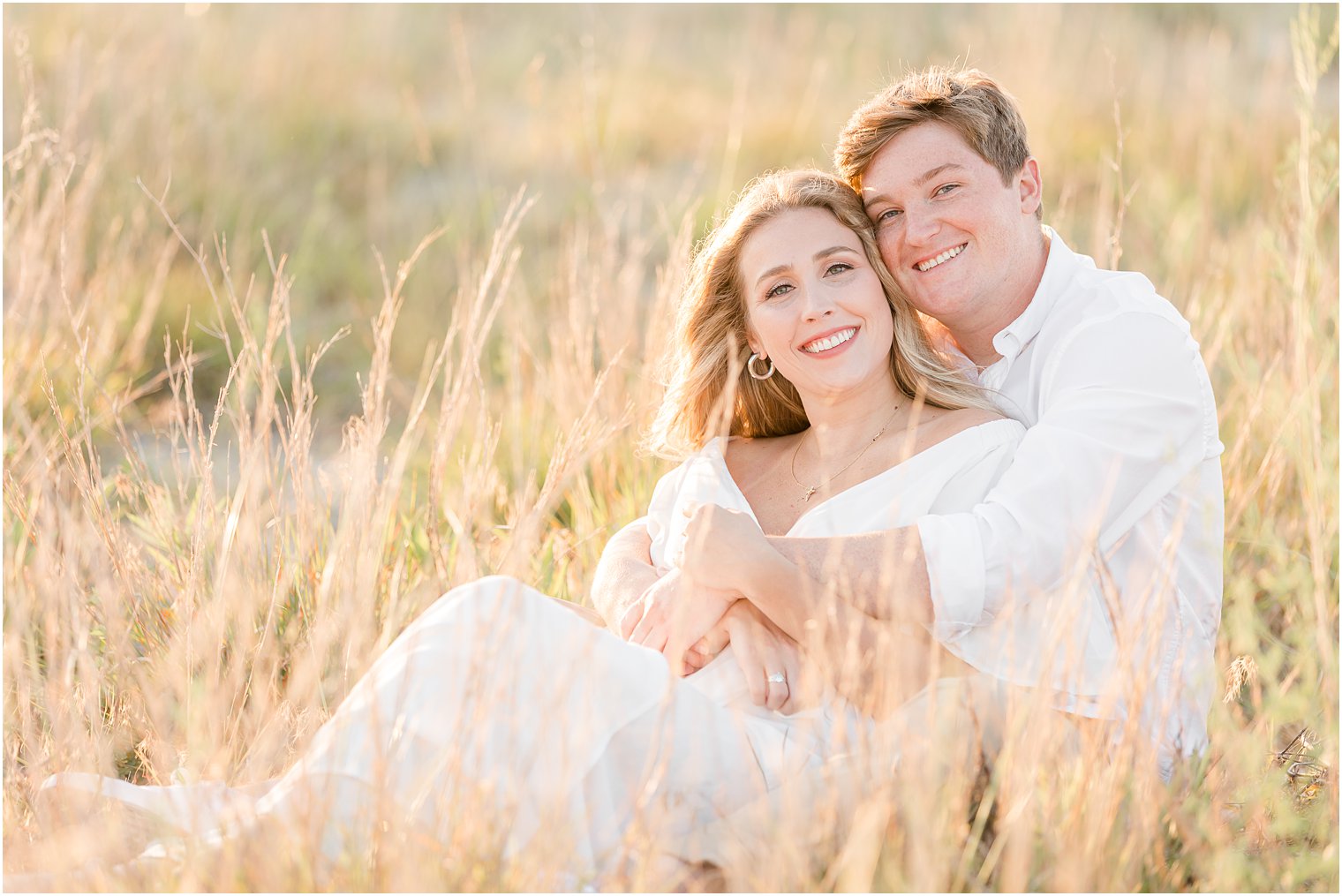 bride and groom sit in tall field at sunset during Long Beach Island engagement photos 