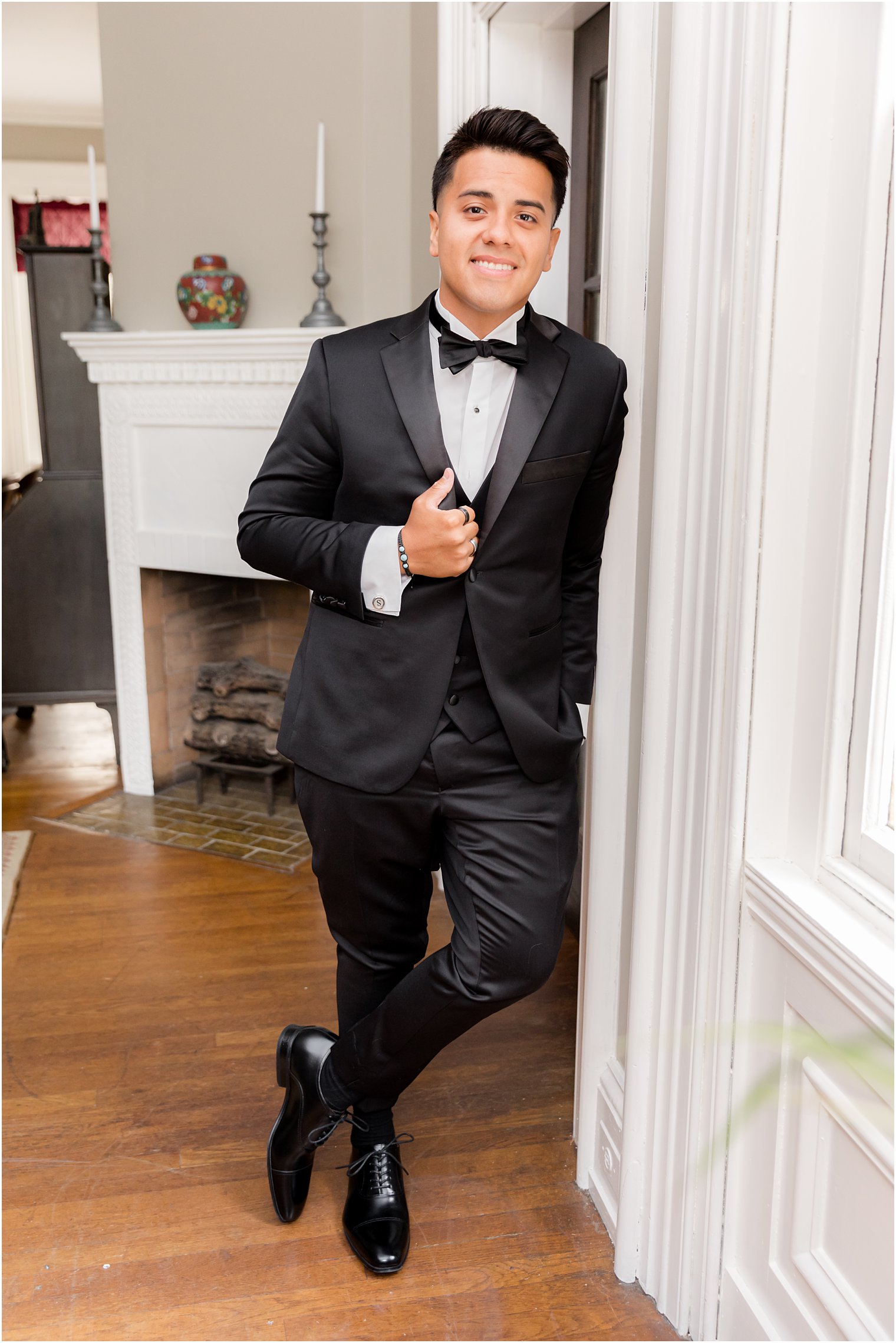 groom leans against doorframe at Collingswood Grand Ballroom in black tux