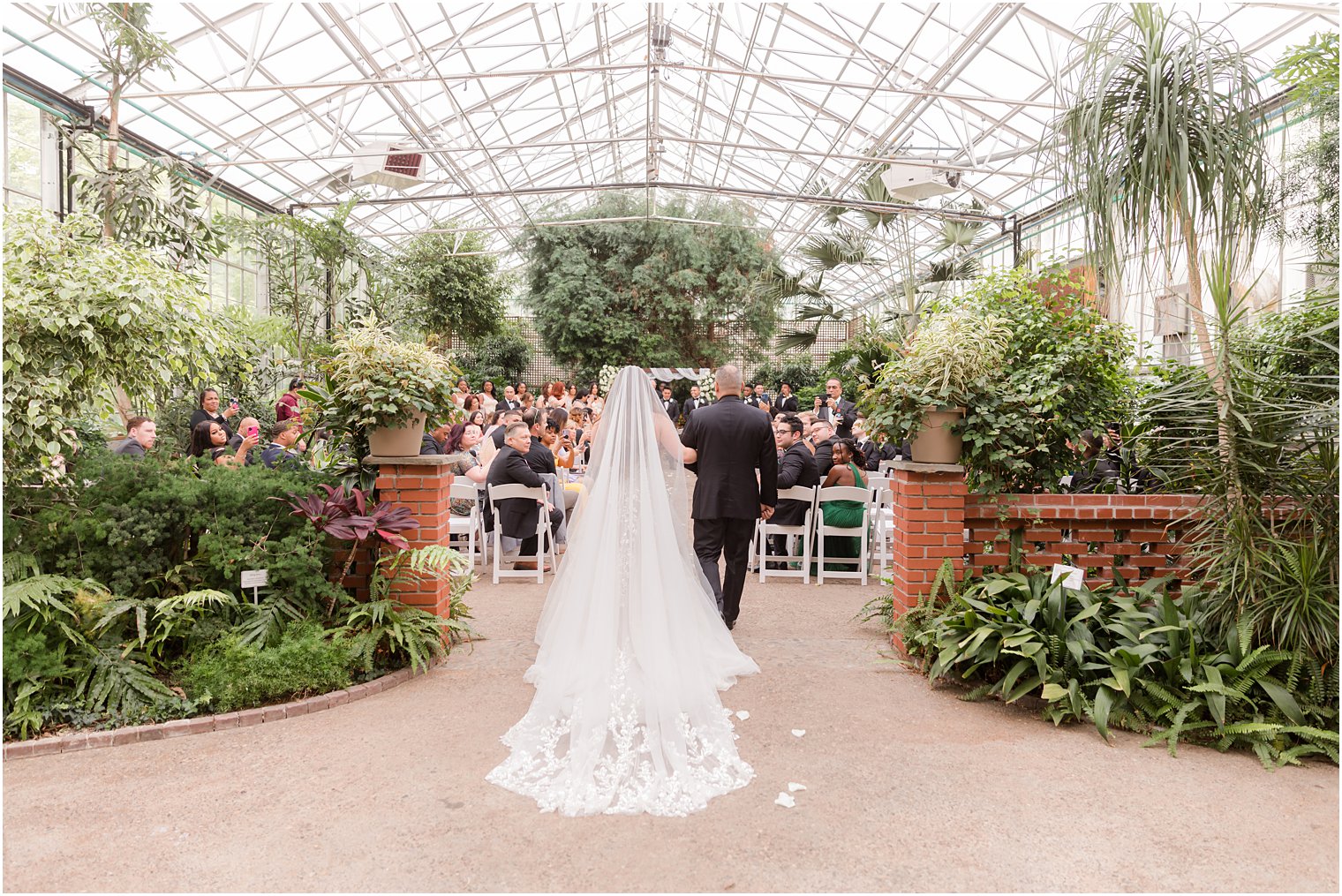 bride walks down aisle with father for Fairmont Park Horticulture Center wedding ceremony