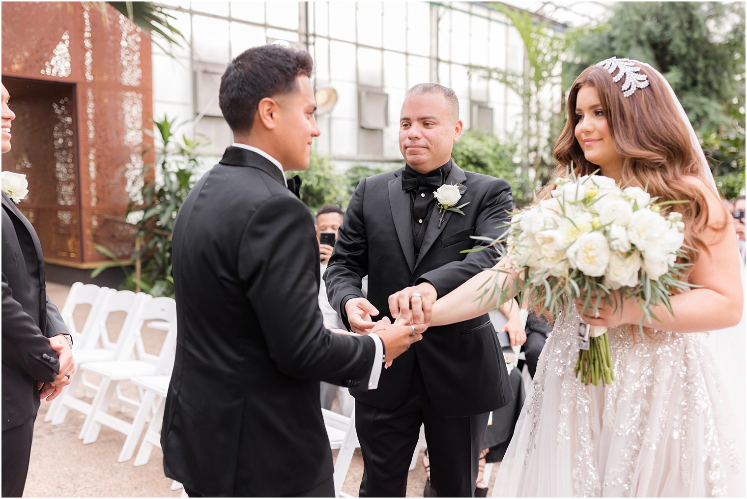 father gives bride's hand to groom during Fairmont Park Horticulture Center wedding ceremony