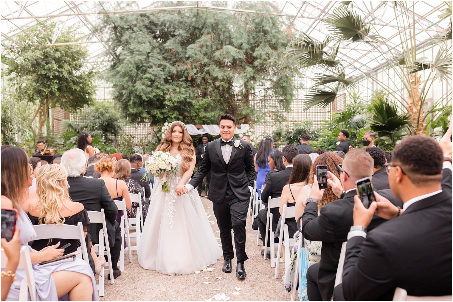 couple holds hands walking up aisle after Fairmont Park Horticulture Center wedding ceremony