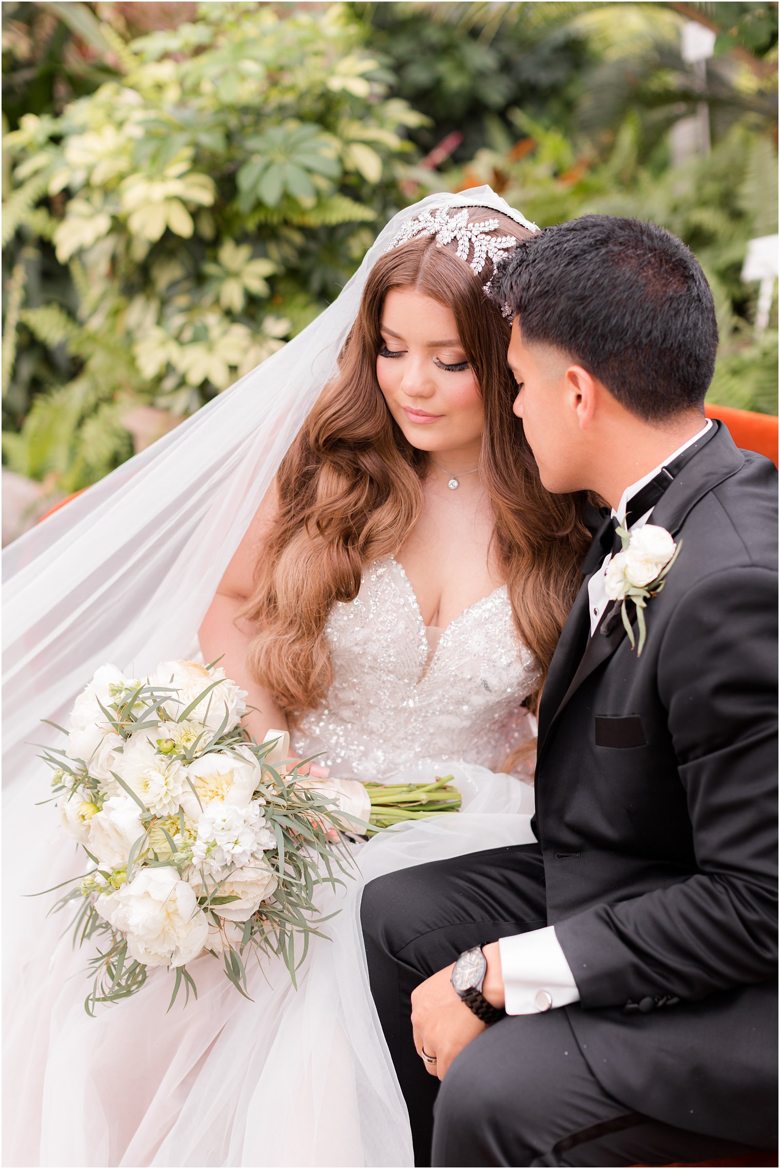 groom looks at bride sitting on orange sofa at Fairmont Park Horticulture Center 