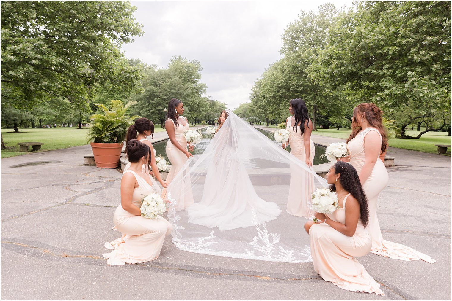 bridesmaids hold veil out for bride by fountain at Fairmount Park Horticulture Center