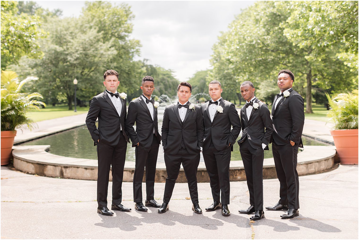 groom and groomsmen pose by fountain in black suits at Fairmount Park Horticulture Center