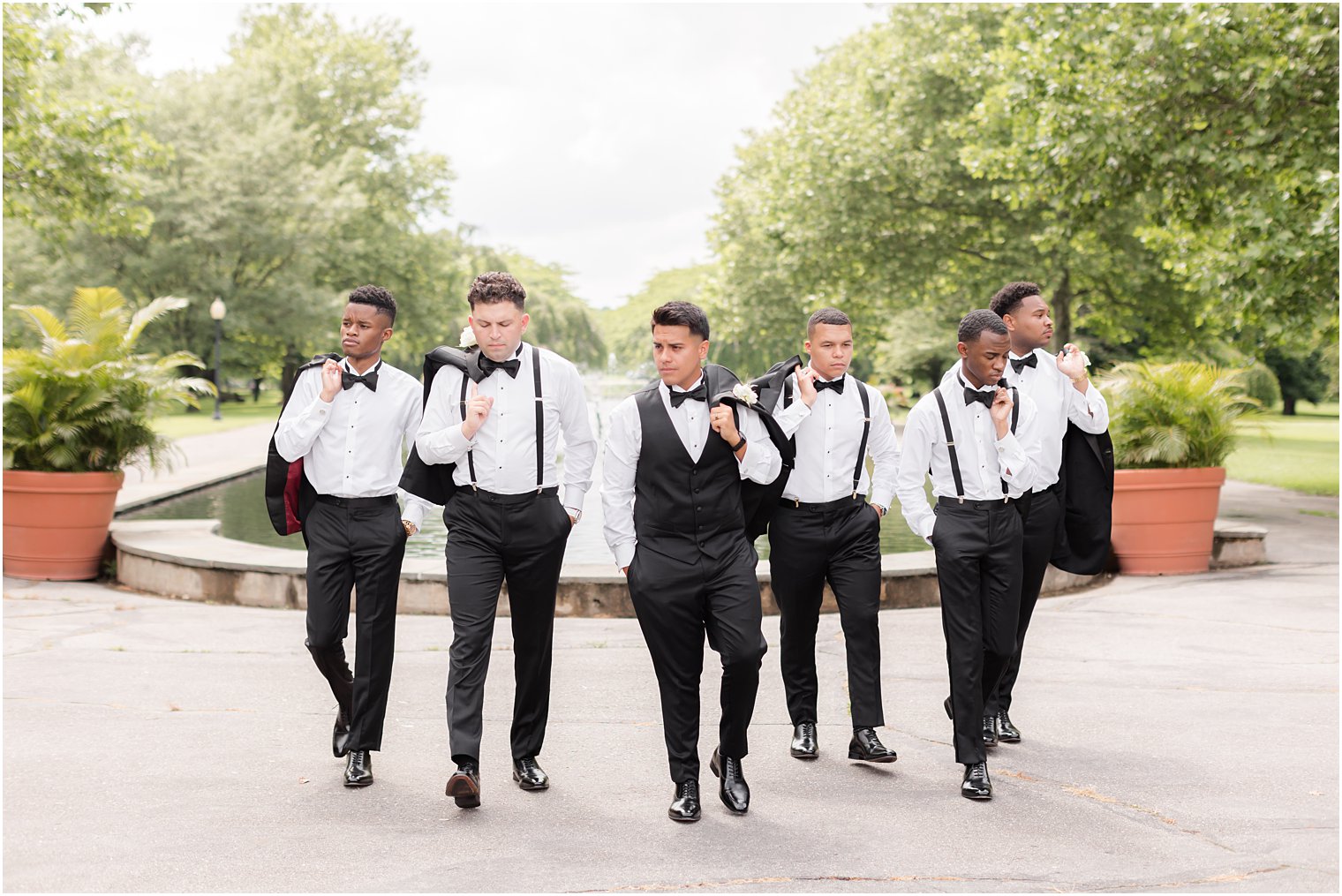 groom and groomsmen walk by fountain with jackets over their shoulders at Fairmount Park Horticulture Center