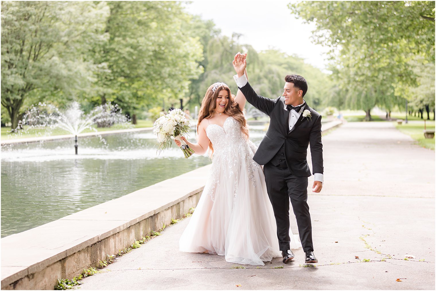 bride and groom bump hips alongside pond at Fairmount Park Horticulture Center