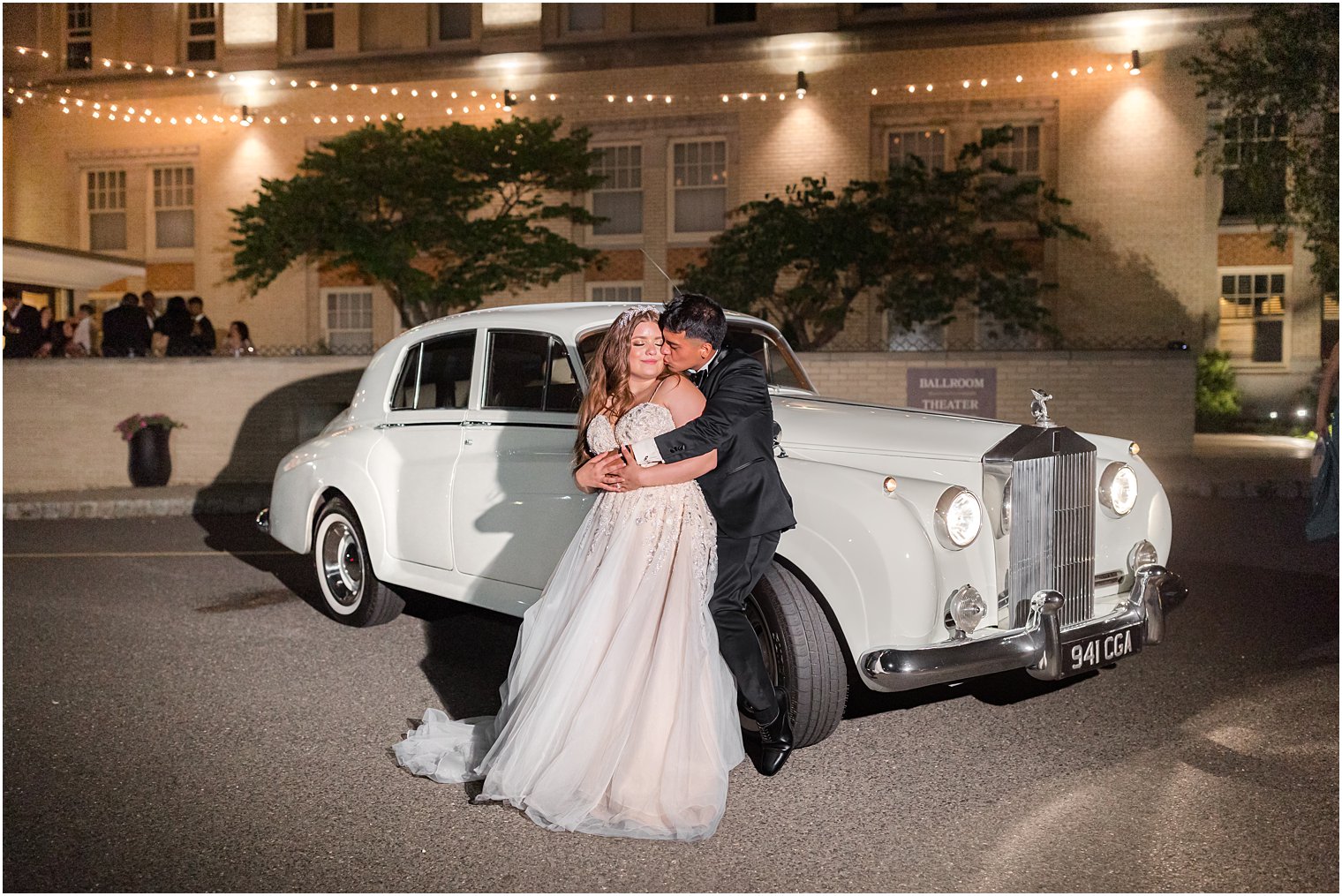 bride and groom hug by classic car outside Collingswood Grand Ballroom