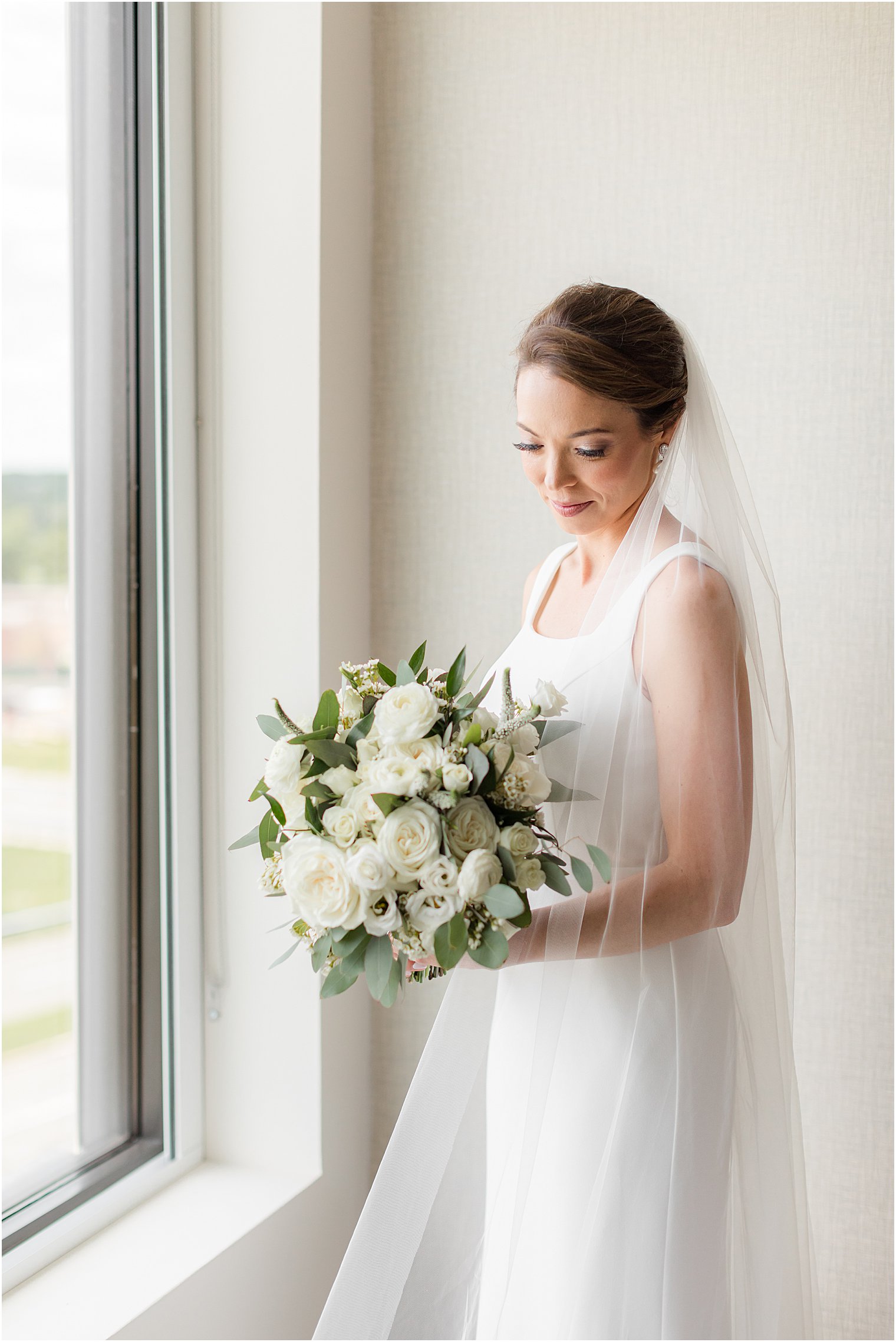 bride looks down at ivory bouquet by window in New Jersey