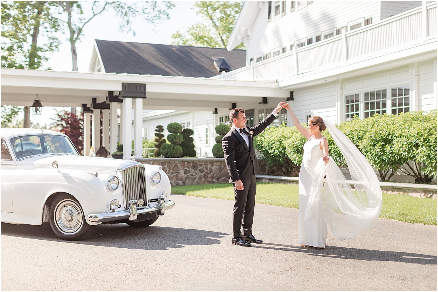 groom twirls bride by classic cars outside Ryland Inn
