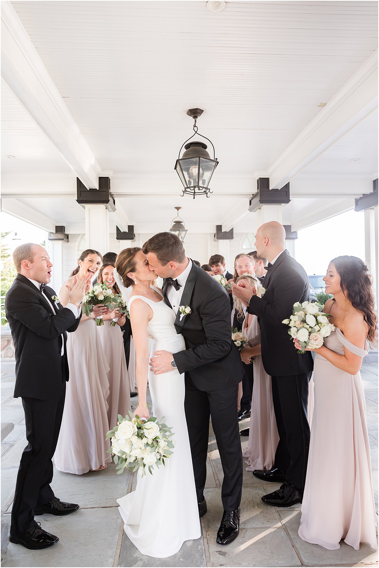 bride and groom kiss with wedding party cheering around them at Ryland Inn