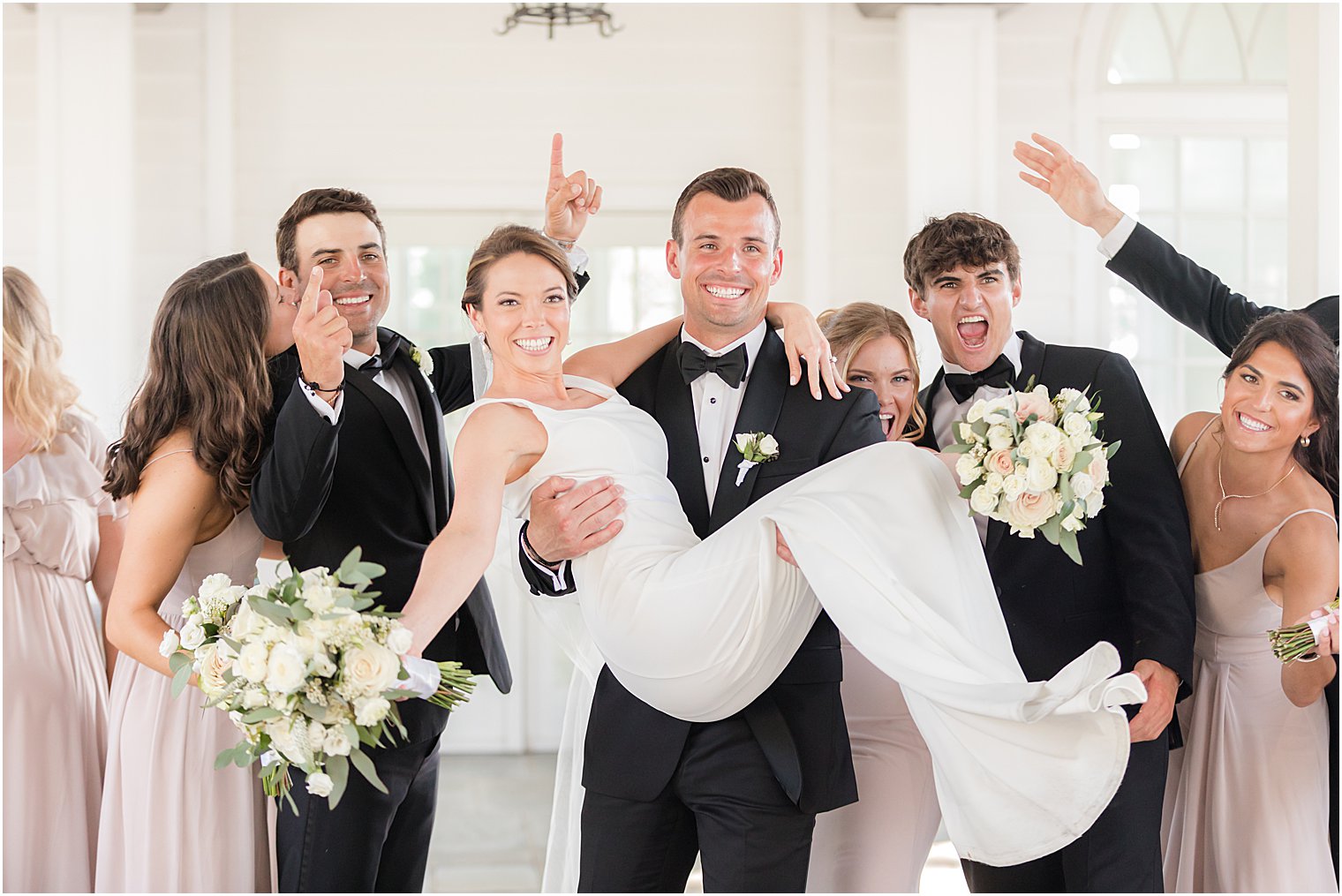 groom carries bride with wedding party outside Ryland Inn