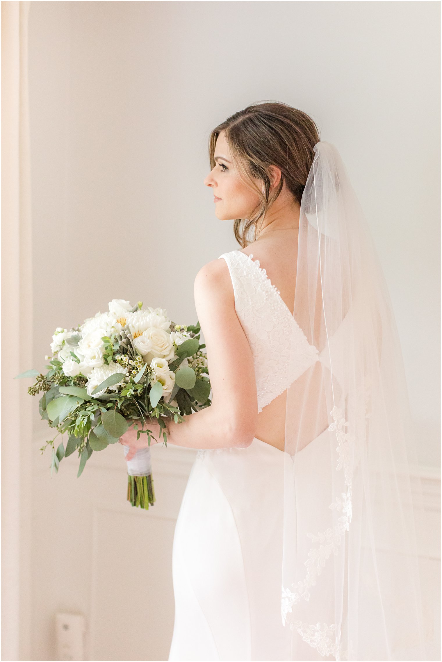 bride looks over shoulder holding bouquet of white flowers