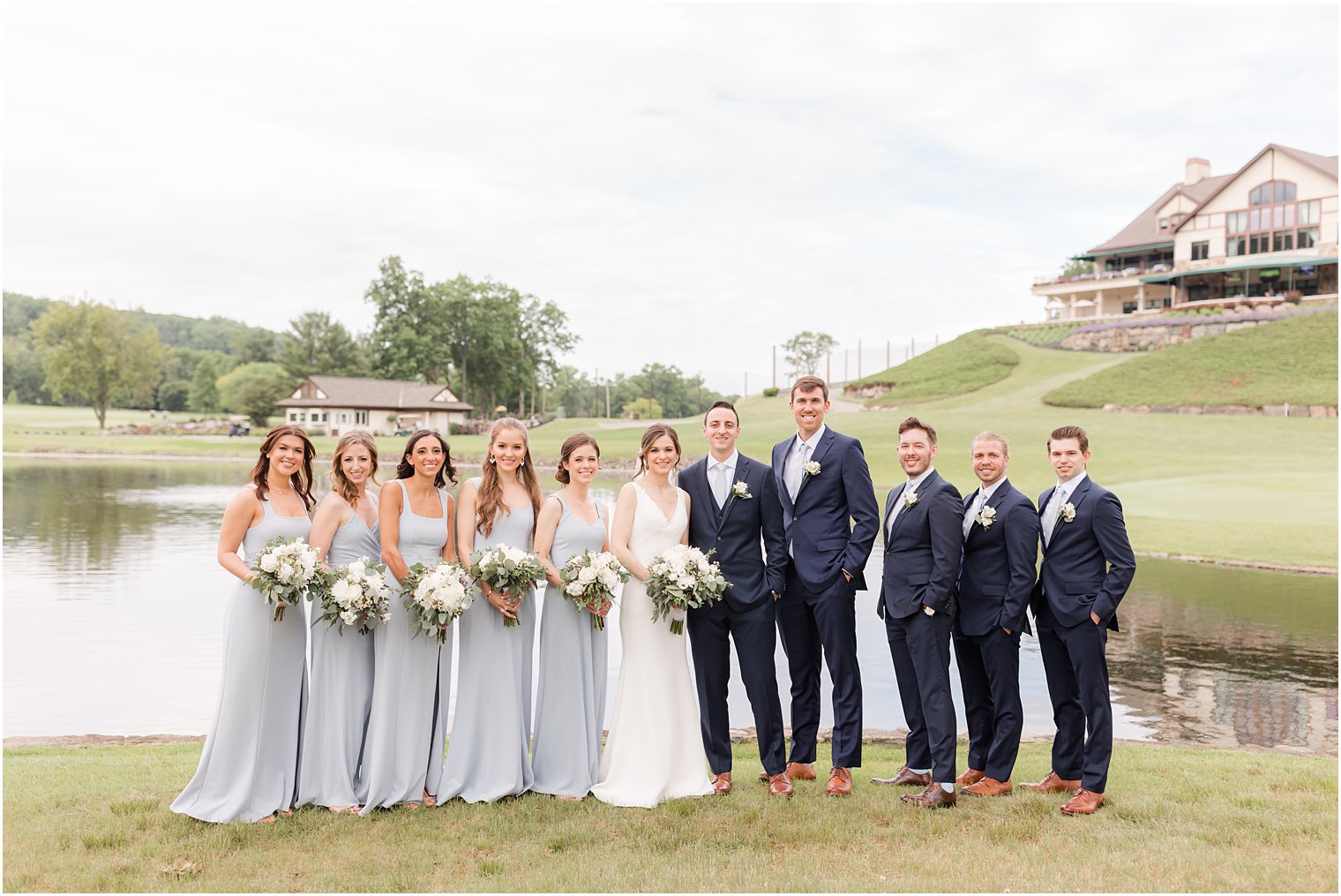 newlyweds pose with wedding party in navy and light blue outside Spring Brook Country Club
