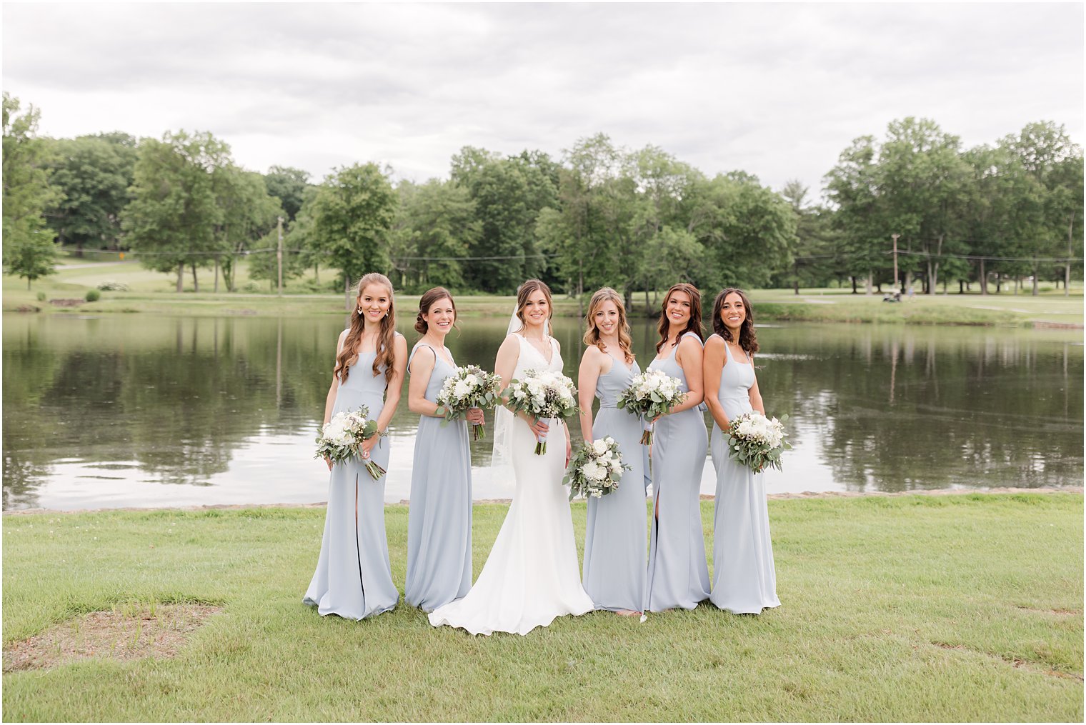 bridesmaids in light blue gowns pose with bride by lake at Spring Brook Country Club
