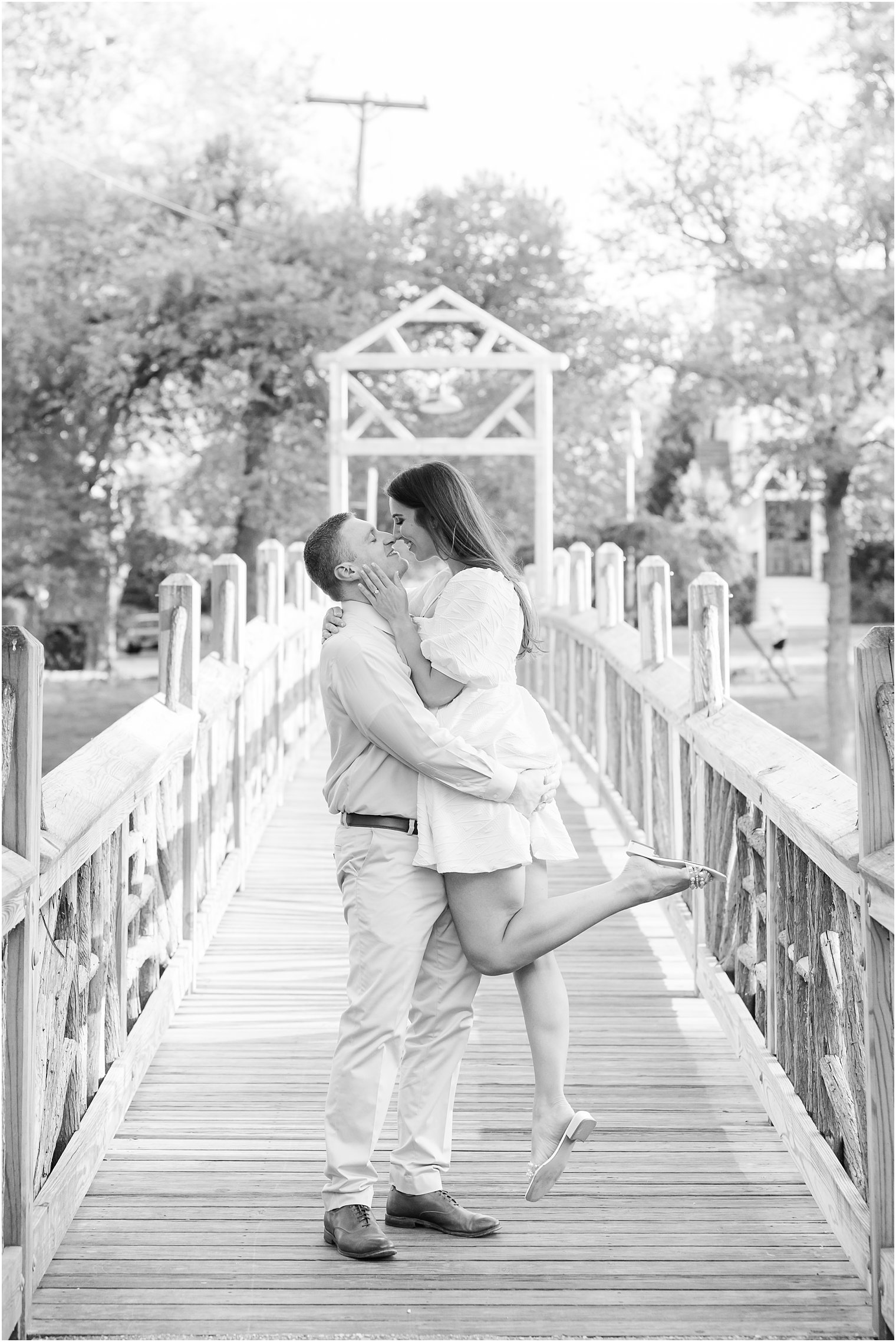 man lifts fiancee during Spring Lake engagement session on wooden bridge 