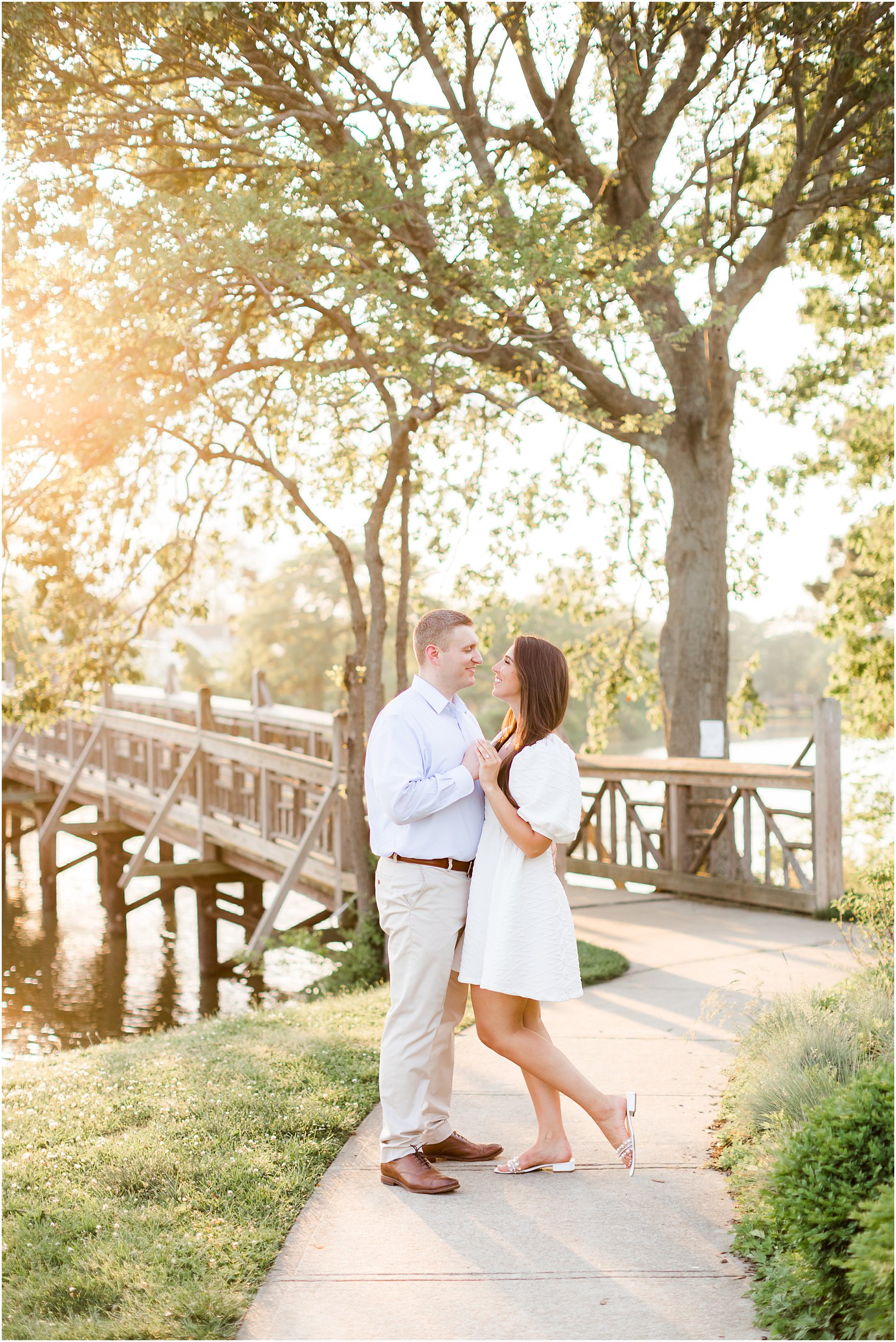 engaged couple poses by bridge at sunset during Spring Lake engagement session