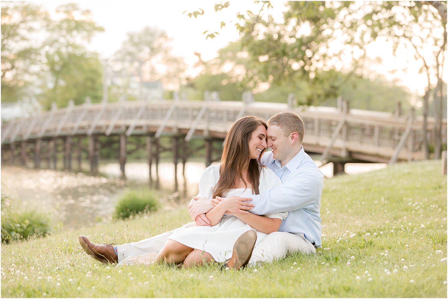 couple sits in grass during summertime engagement photos