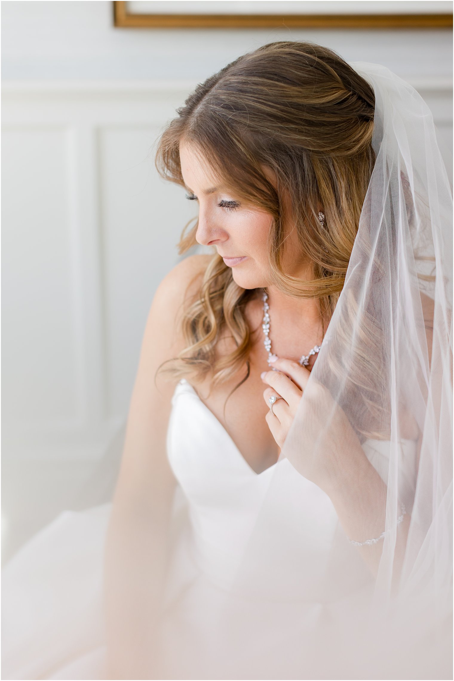 bride holds necklace looking over shoulder with veil around her