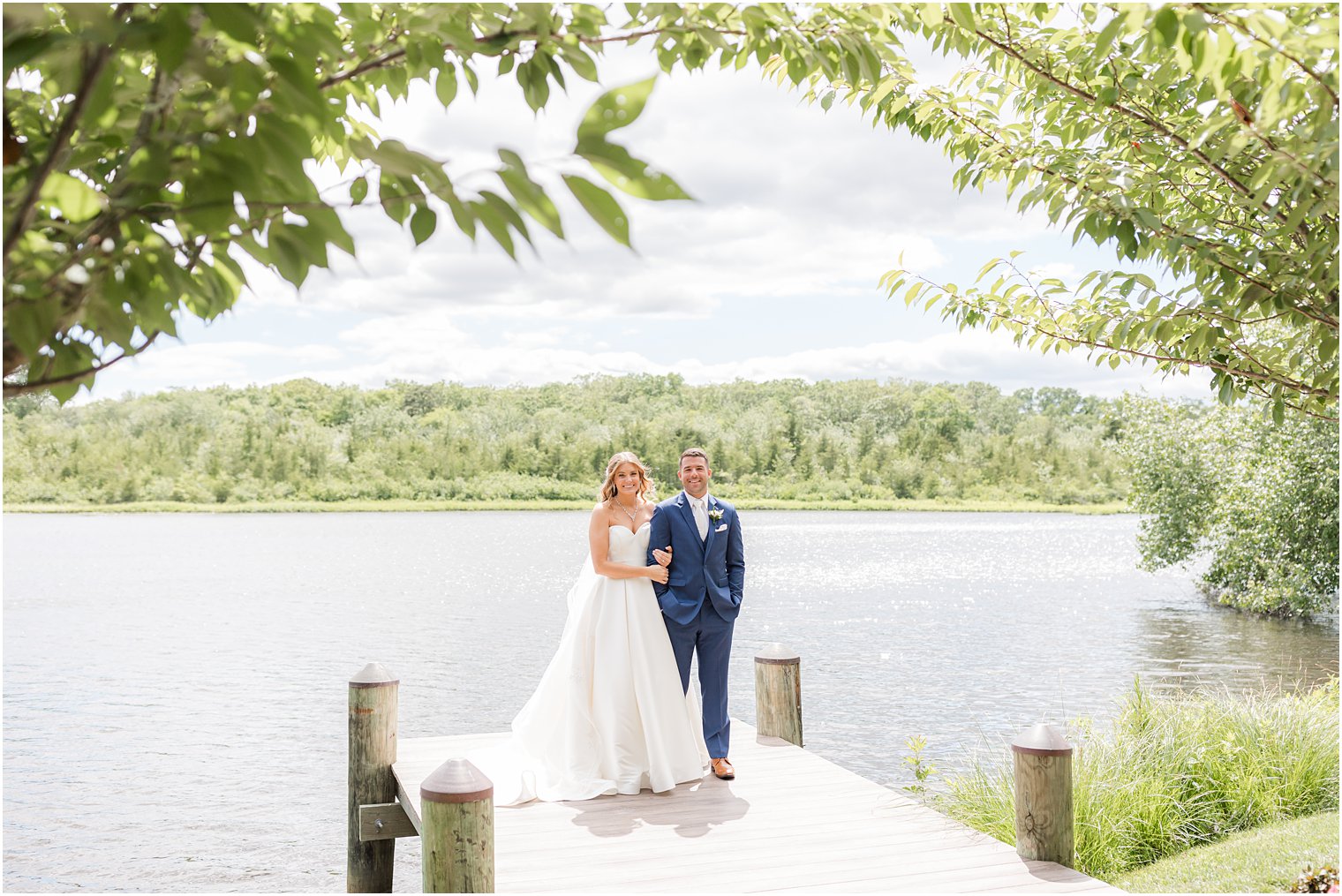 newlyweds stand on dock at The Mill Lakeside Manor with bride holding groom's arm in navy suit