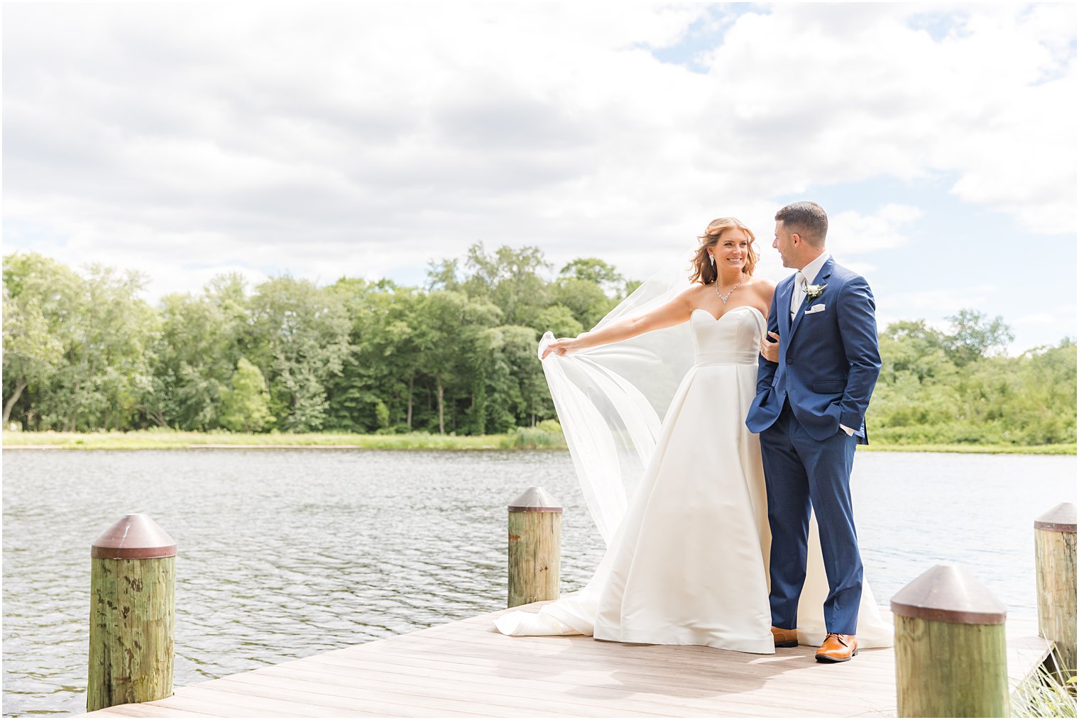 bride holds out veil while couple stands on dock in New Jersey 