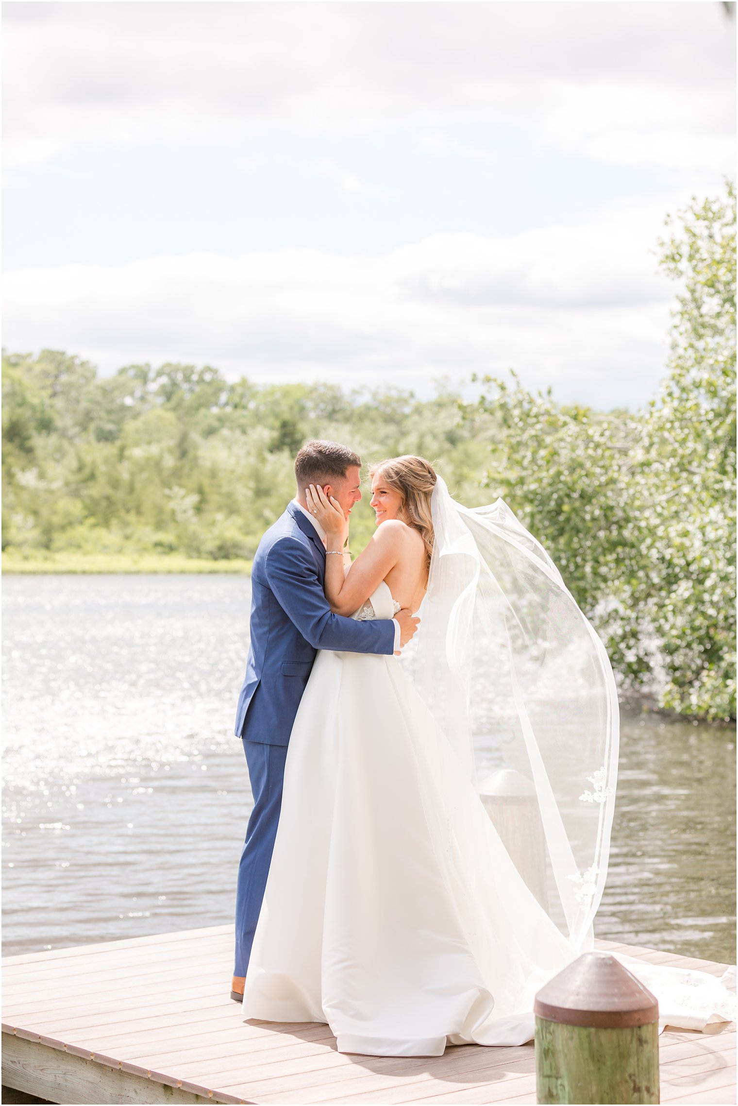 couple laughs while bride's veil moves in wind on dock 