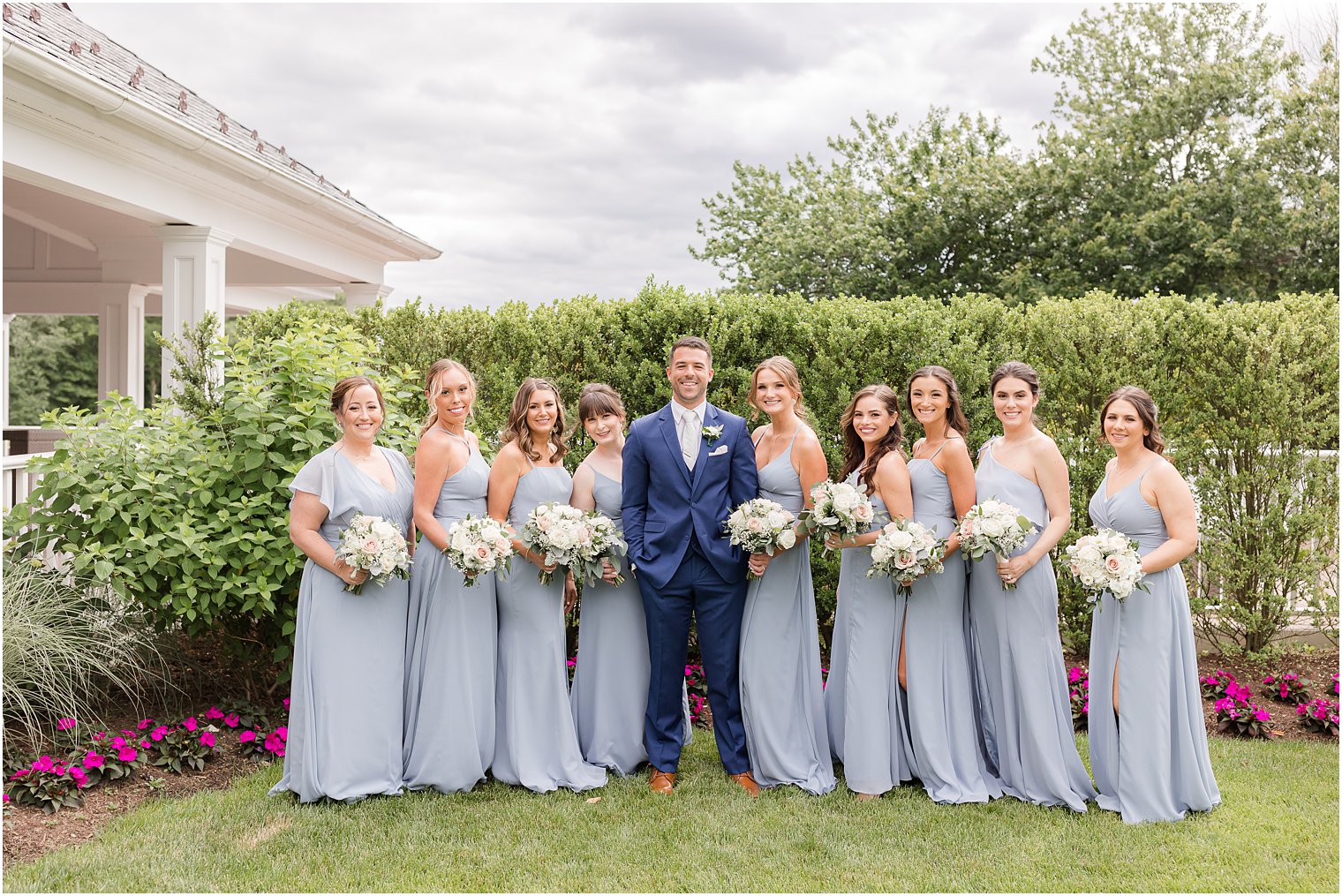 groom poses with bridesmaids in pastel blue gowns outside The Mill Lakeside Manor