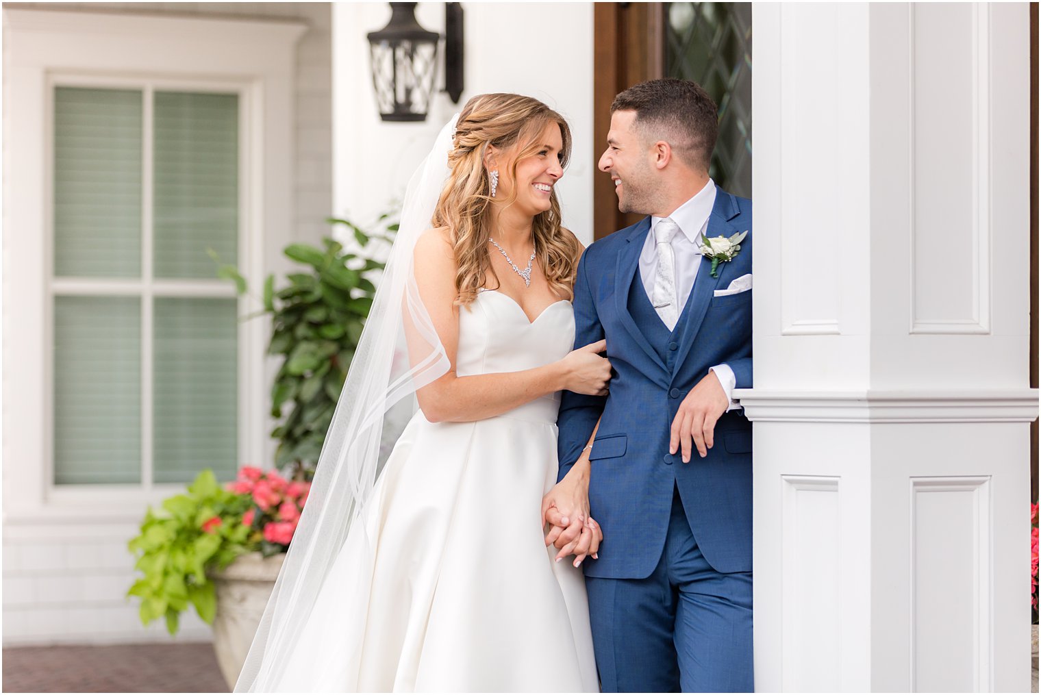 bride holds onto groom's arm while he leans against column at The Mill Lakeside Manor