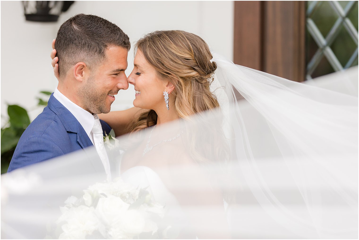 bride and groom lean noses together with bride's veil floating around them