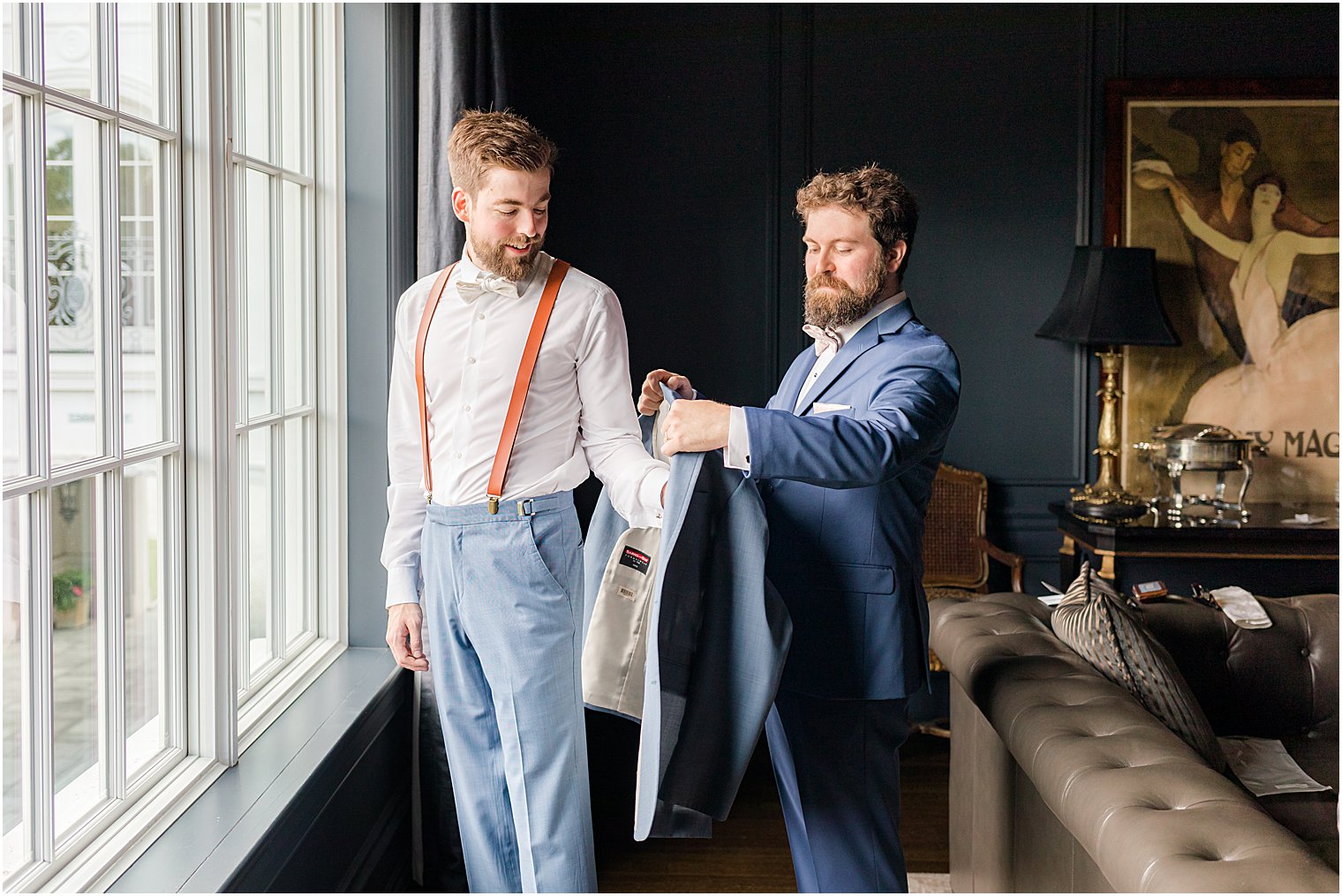 groomsman in navy jacket helps groom into jacket