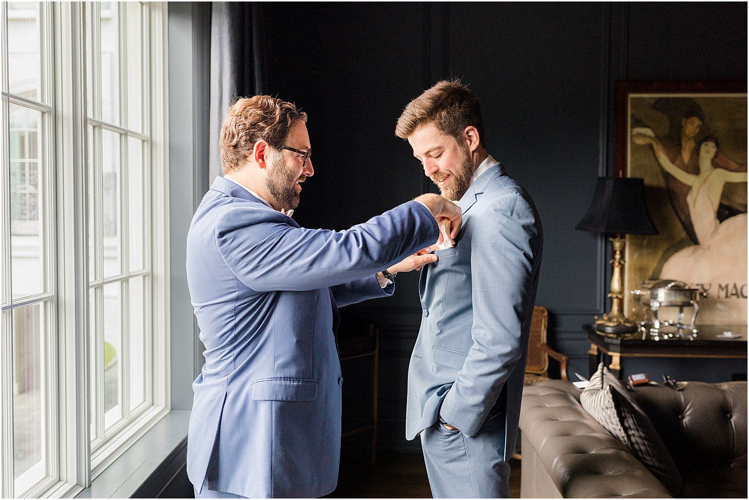 groomsman adjusts tie for groom during wedding day prep