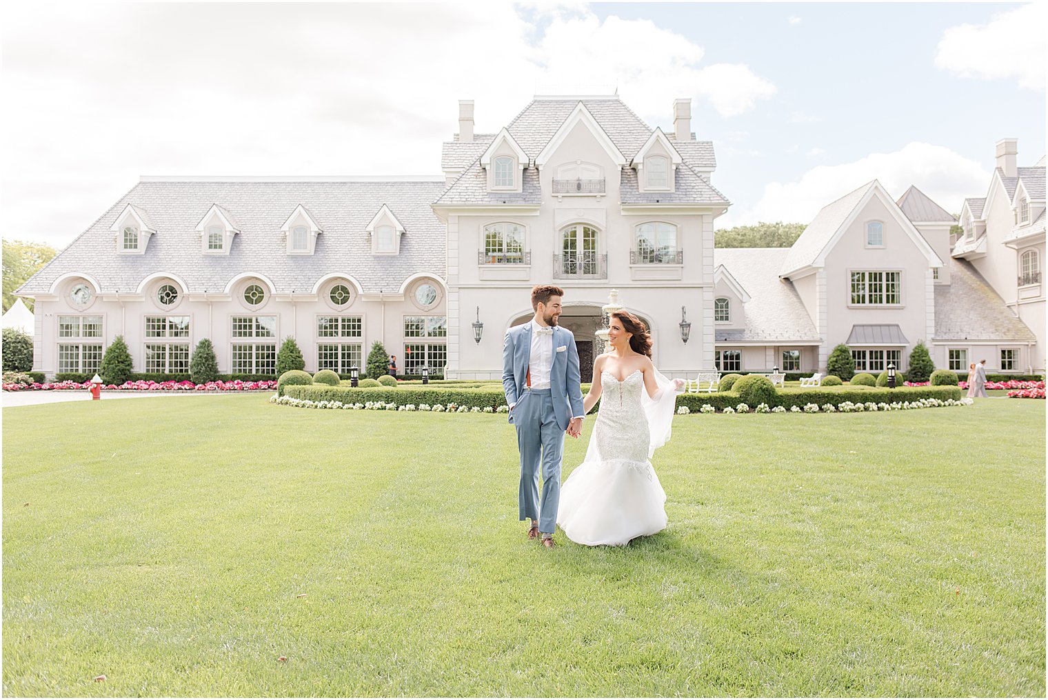 newlyweds hold hands walking on lawn during portraits at Park Chateau Estate