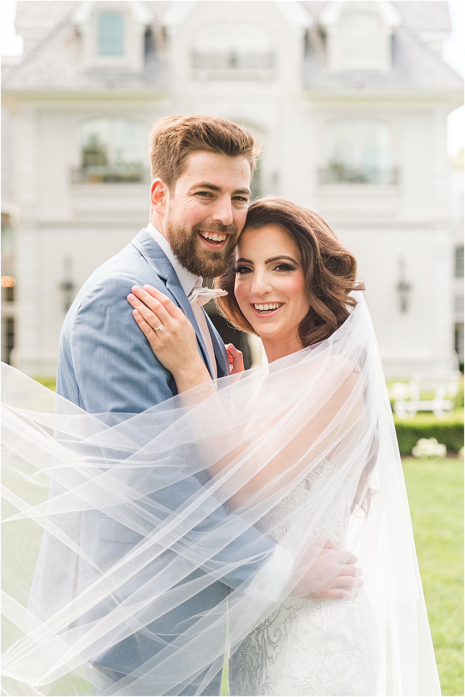 husband and wife hug with bride's veil around their shoulders