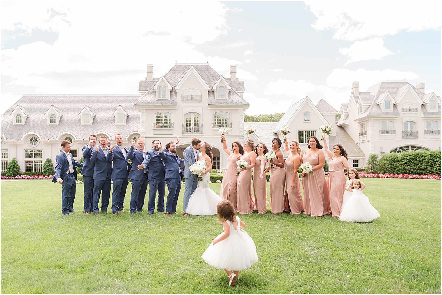 newlyweds kiss with wedding party around them outside Park Chateau Estate