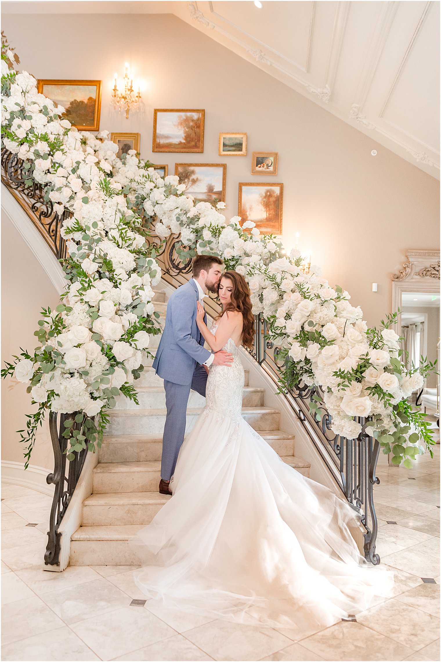 newlyweds stand on staircase lined with white flowers at Park Chateau Estate