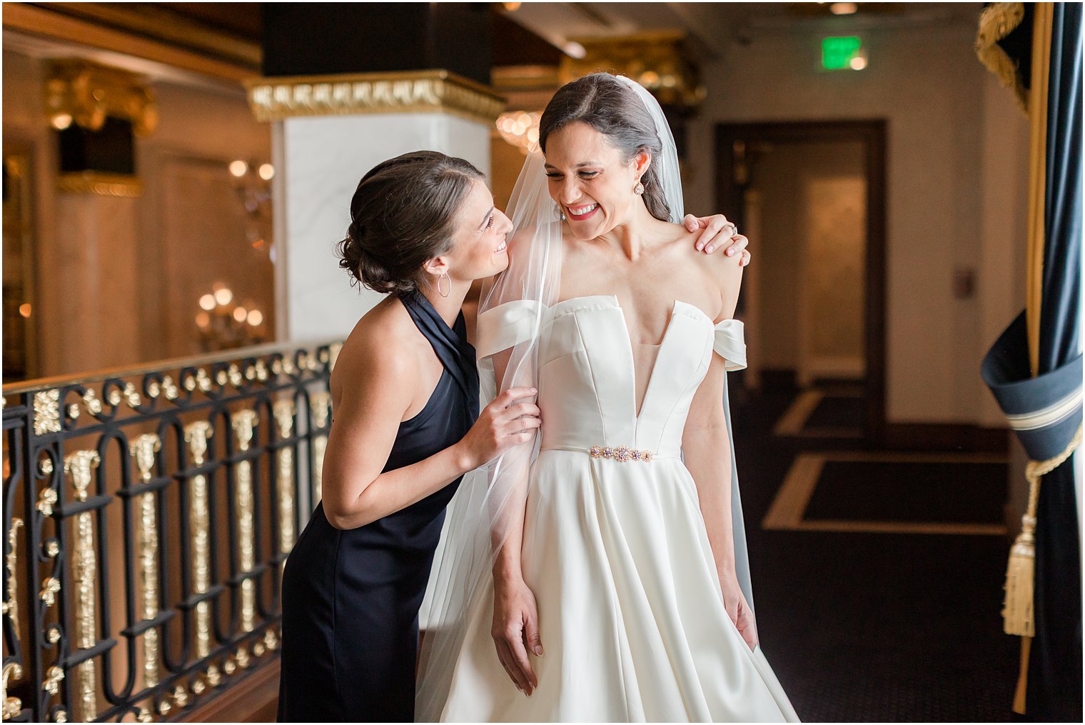 bridesmaid hugs bride while helping with veil