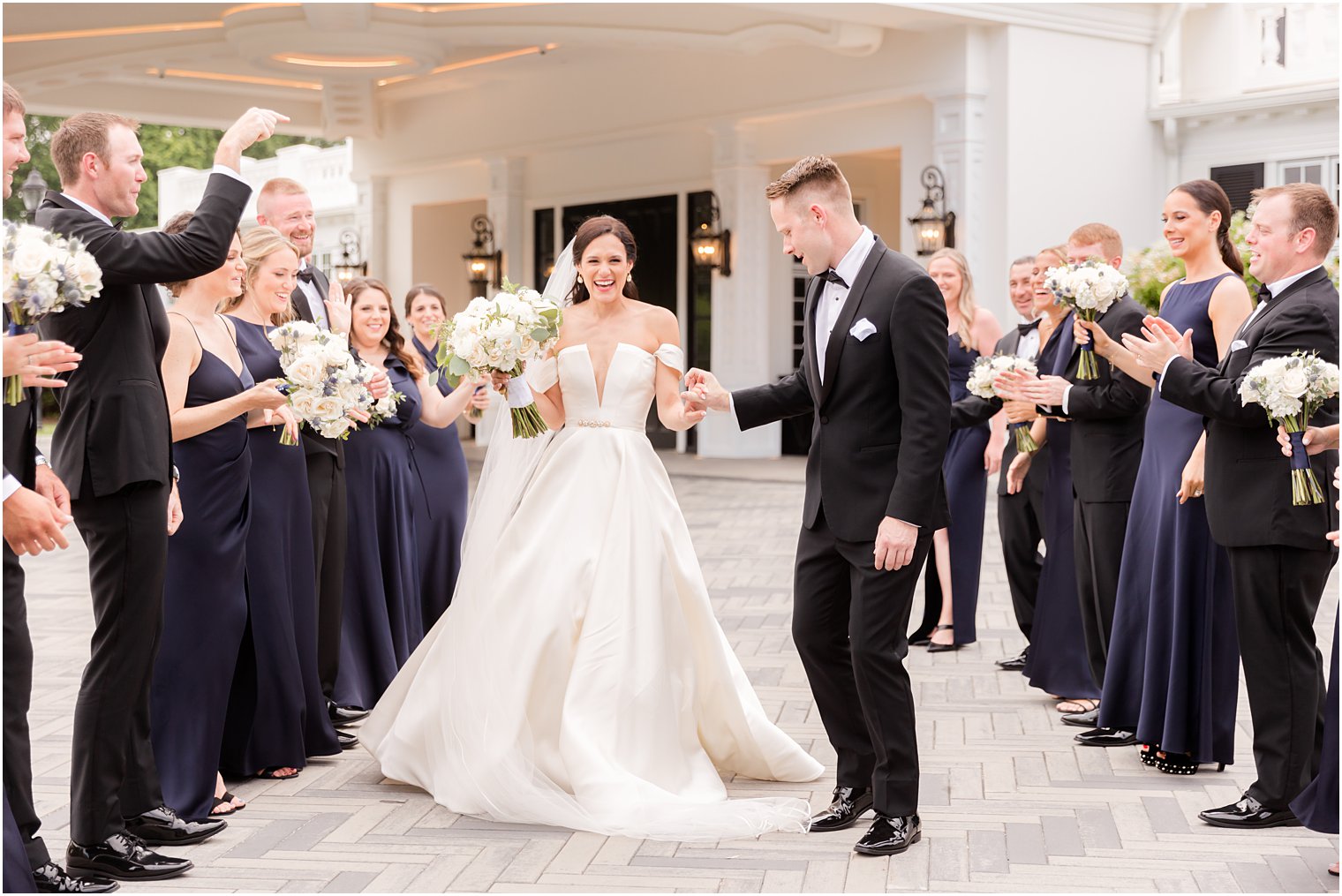 groom holds bride's hand walking between wedding party