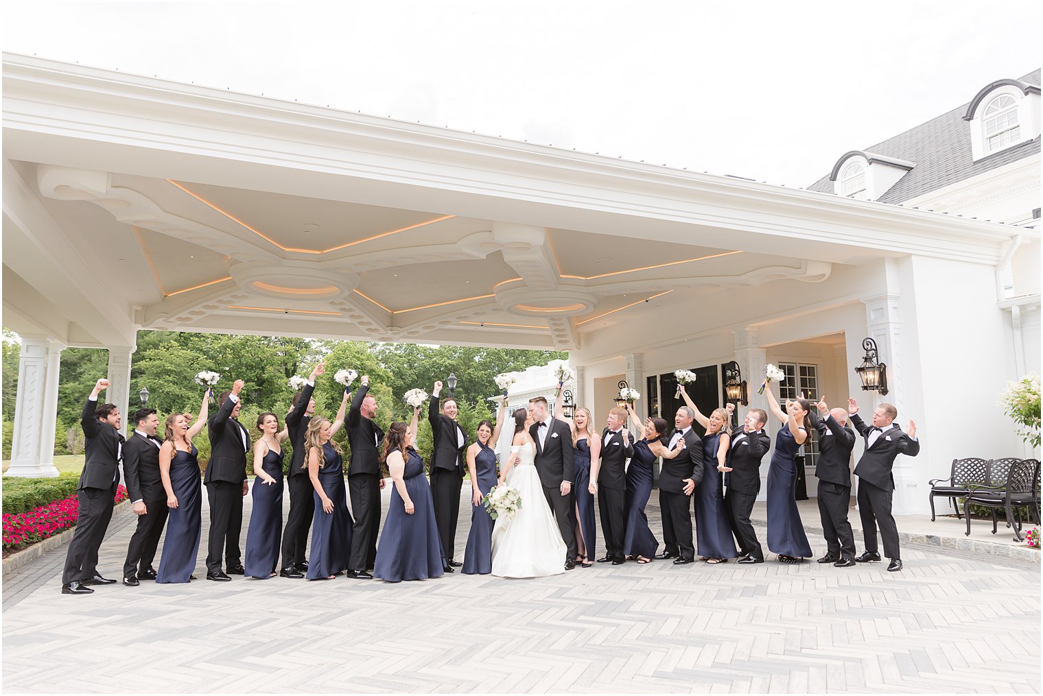 bride and groom kiss with wedding party in navy and black around them
