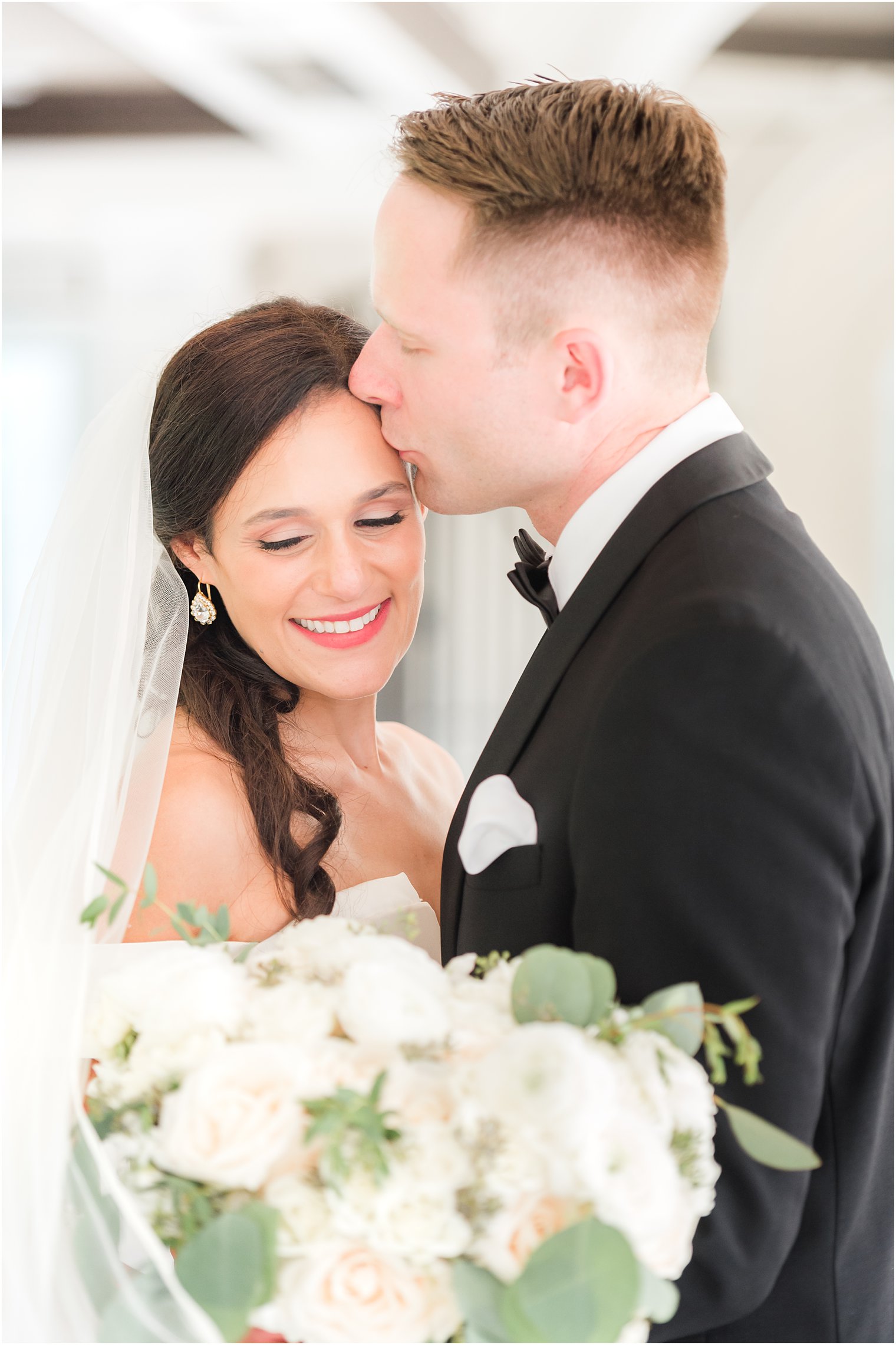 groom kisses bride's forehead while hugging her