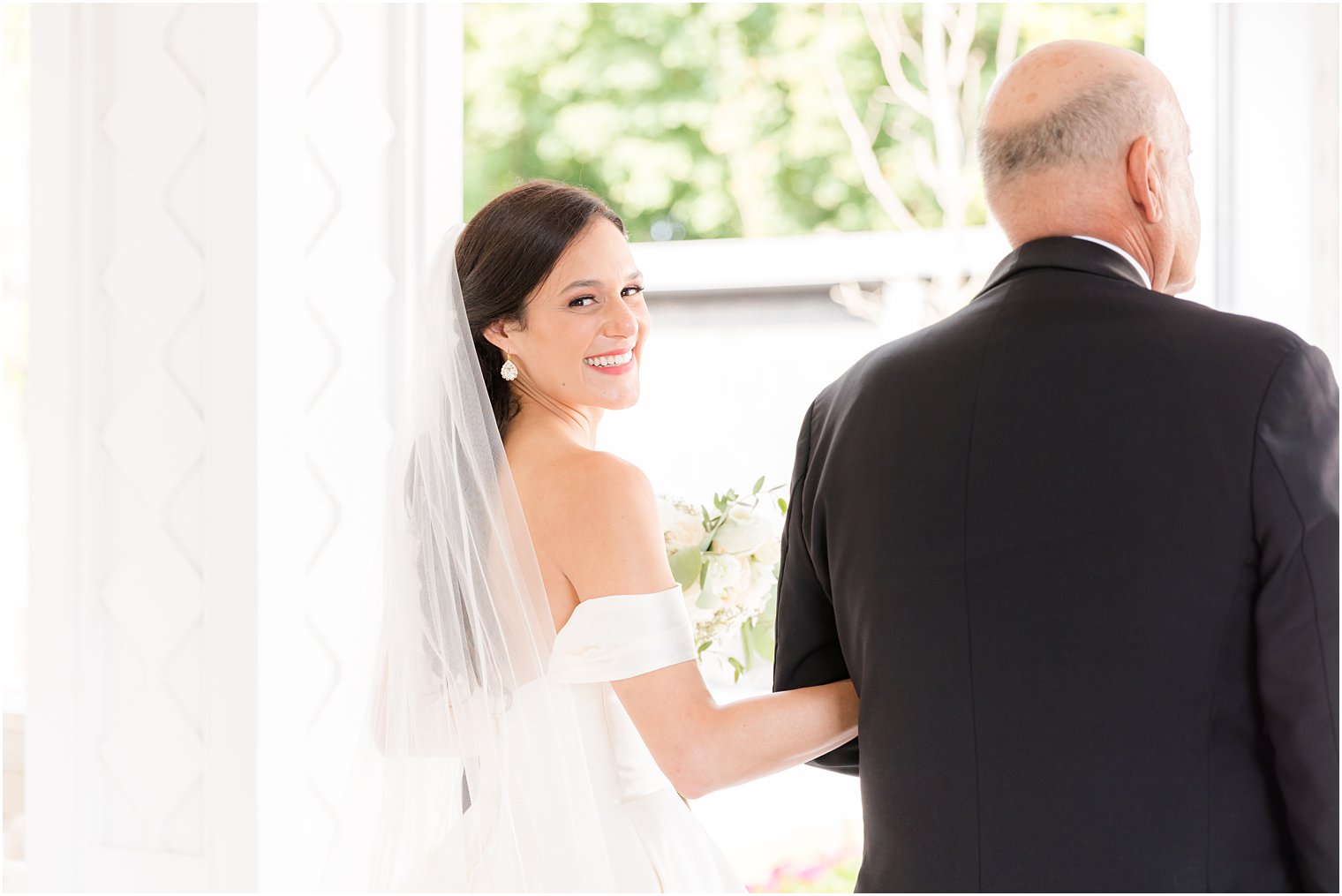 bride looks over shoulder while holding onto dad's arm before NJ wedding ceremony