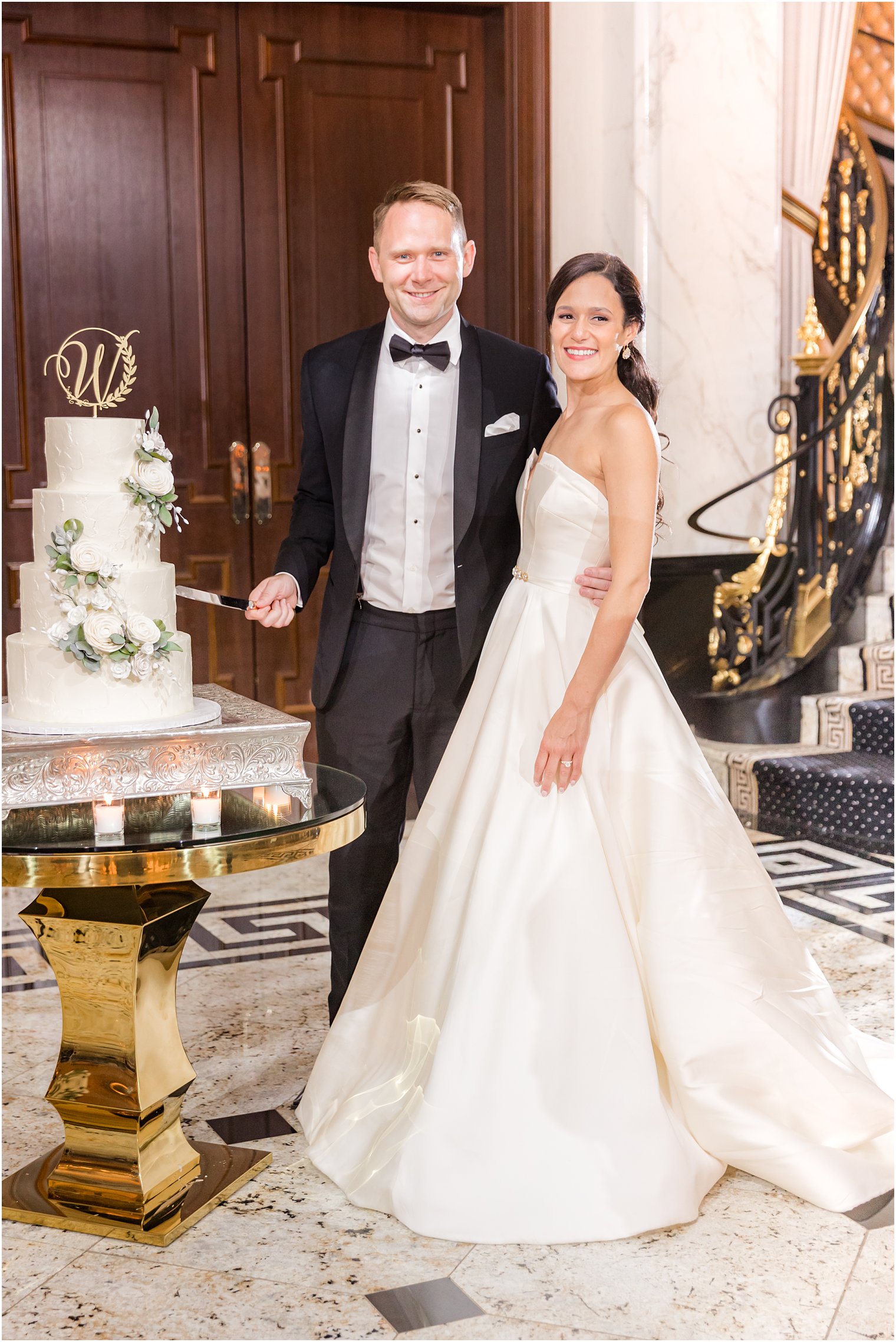 bride and groom stand with wedding cake in ballroom