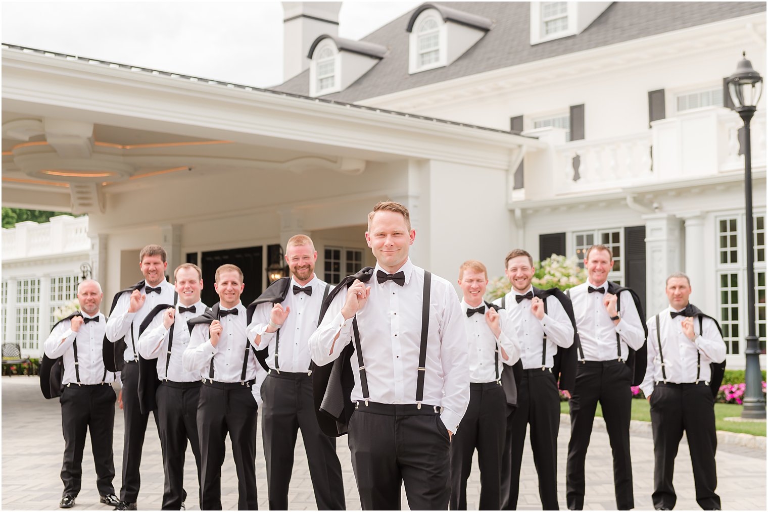 groom flings jacket over shoulder with groomsmen outside Shadowbrook at Shrewbsury