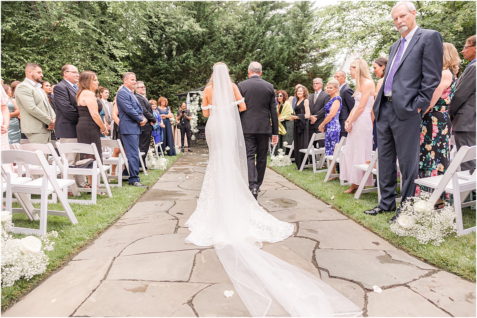bride walks down aisle with veil behind her during Jewish ceremony in the gardens of The English Manor