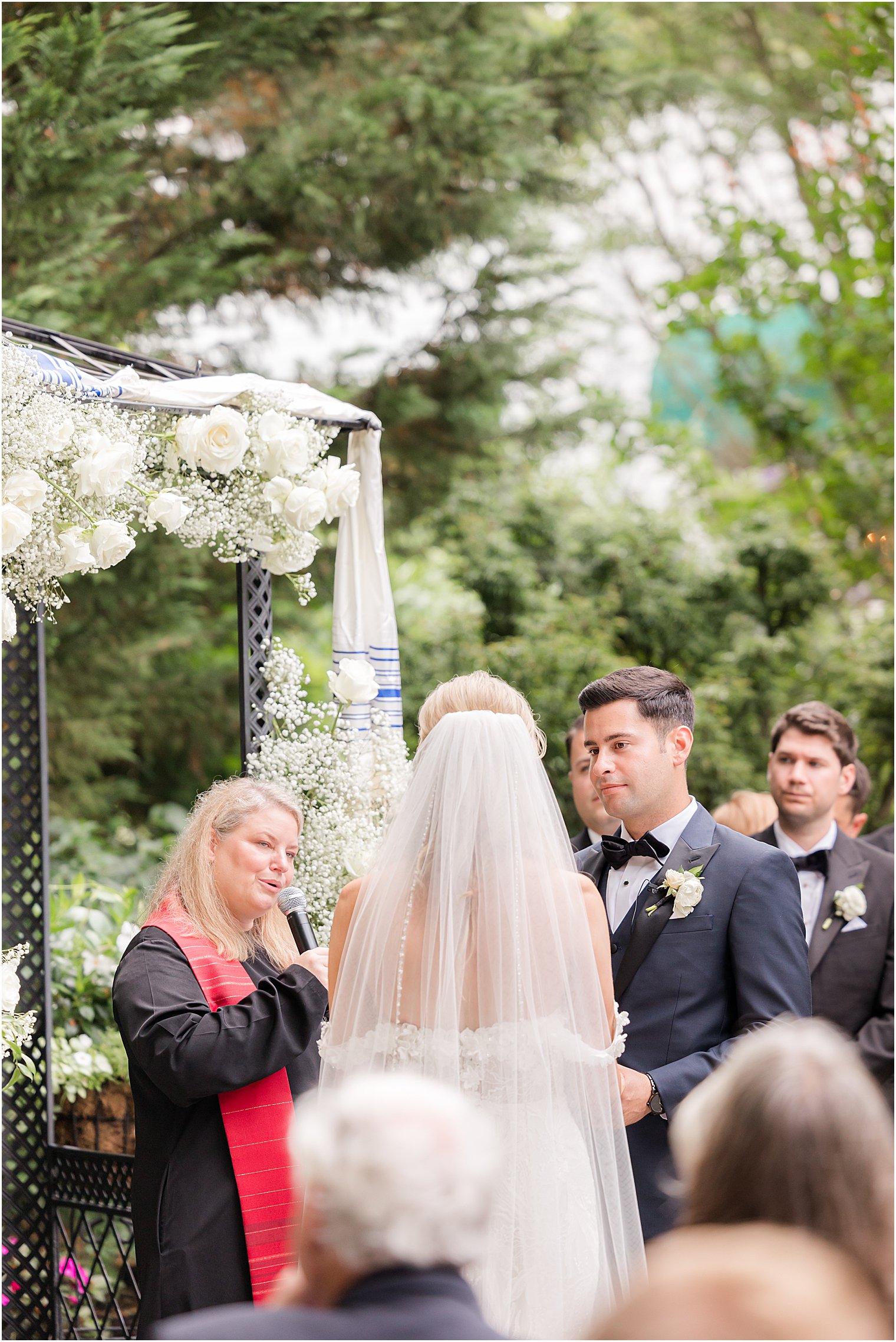 groom looks at bride during Jewish ceremony in the gardens of The English Manor
