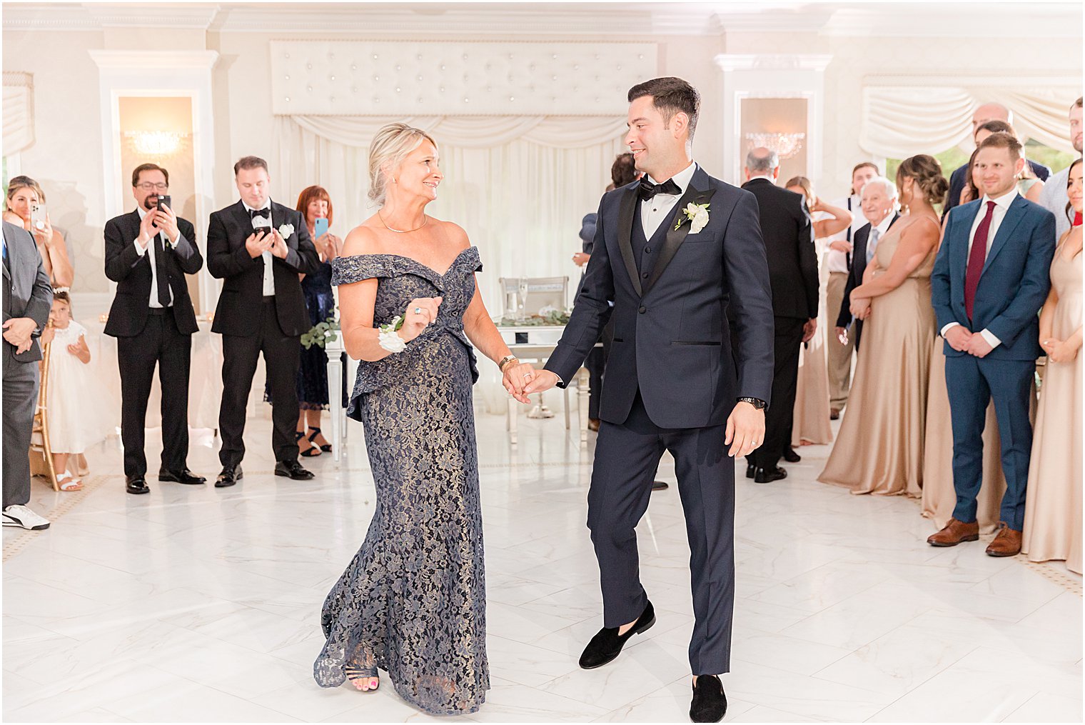 groom and mom hold hands walking on dance floor